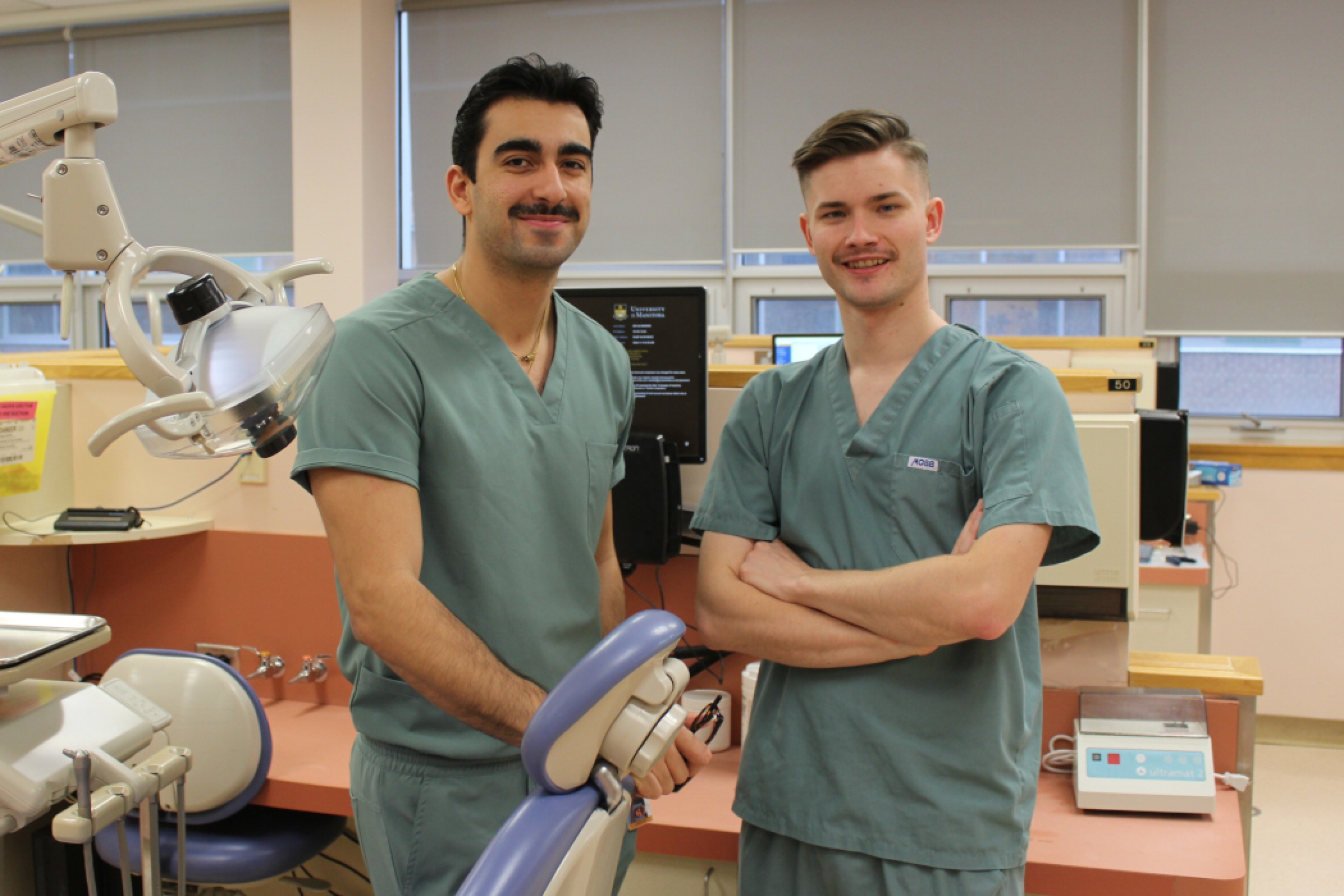 Two students wearing scrubs pose for a photo in a dental clinic.