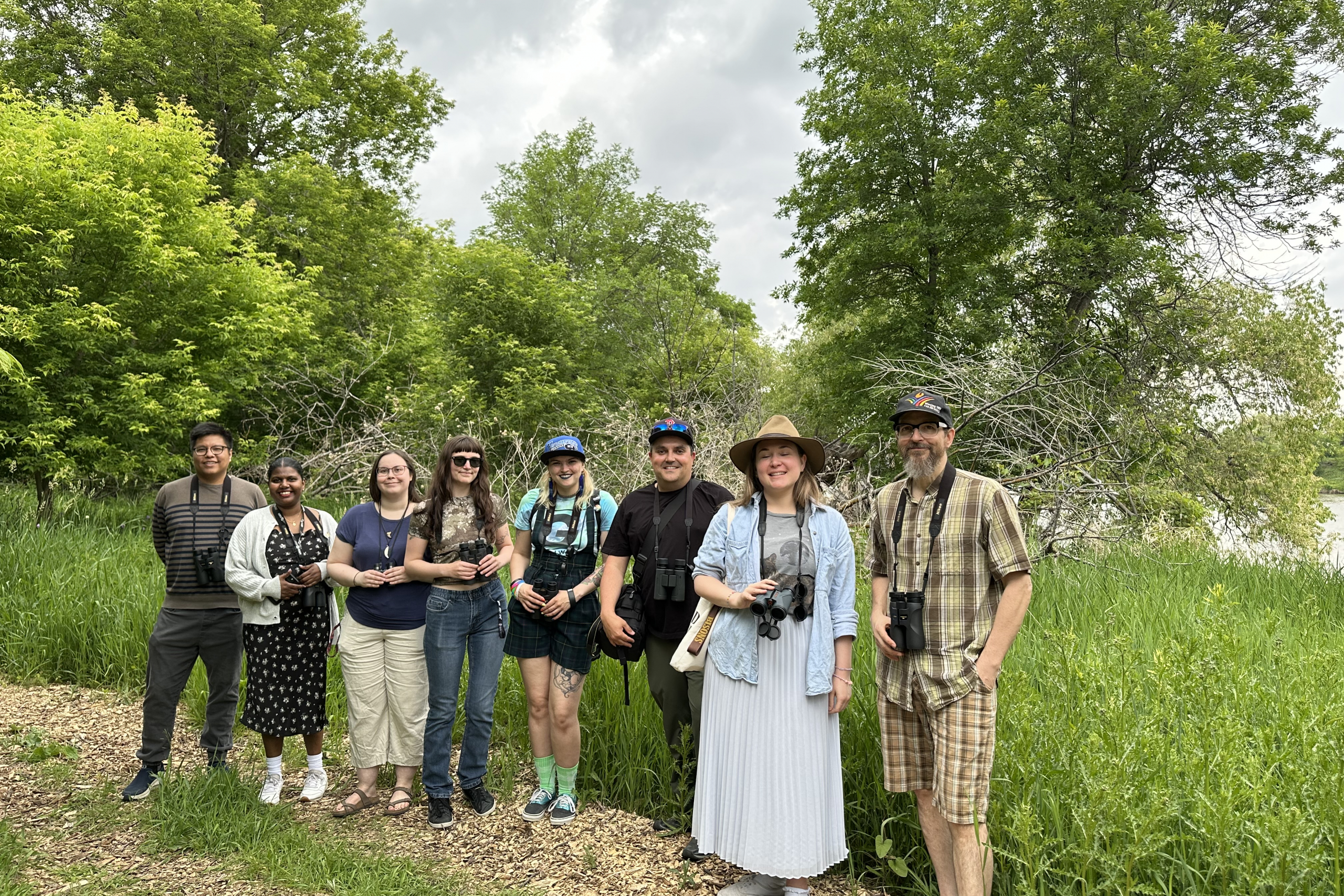 group of people together for a photo in the park, surrounded by trees.