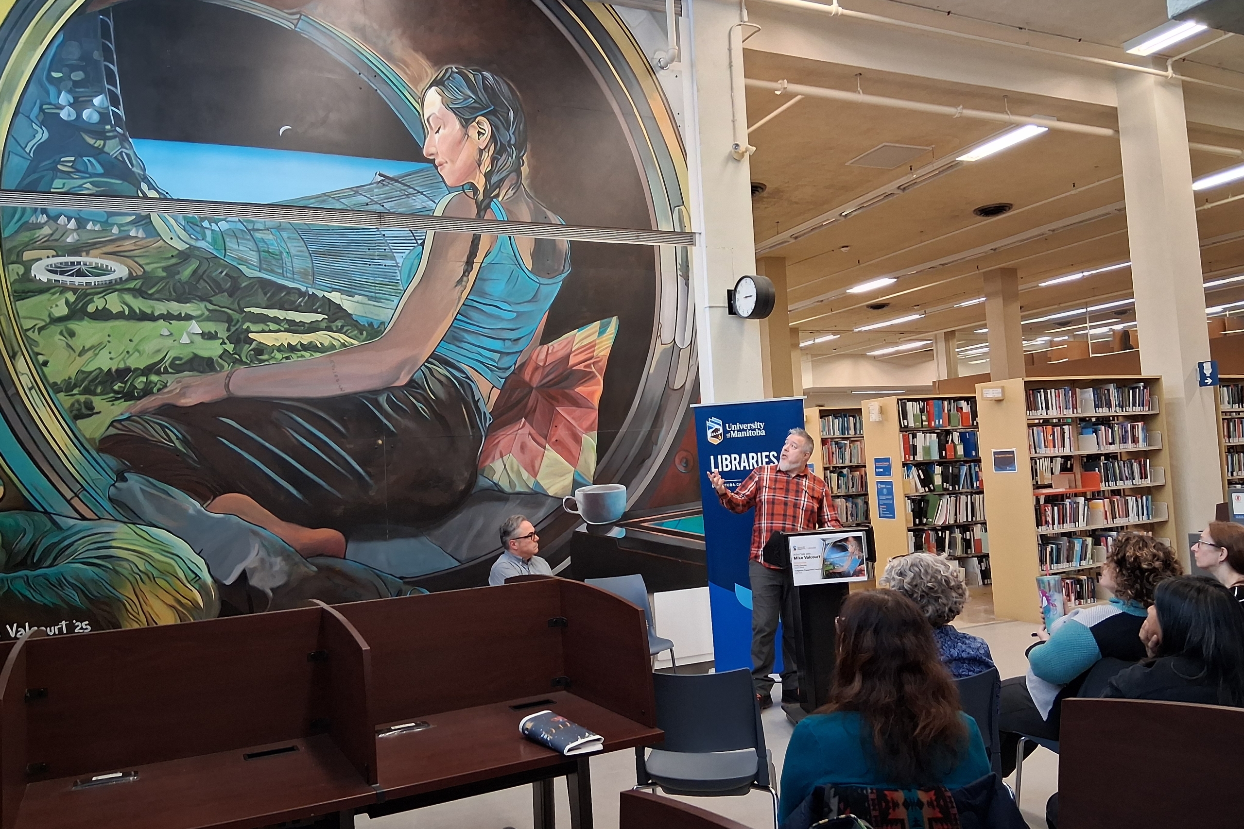 Artist Mike Valcourt presenting in front of his wall mural