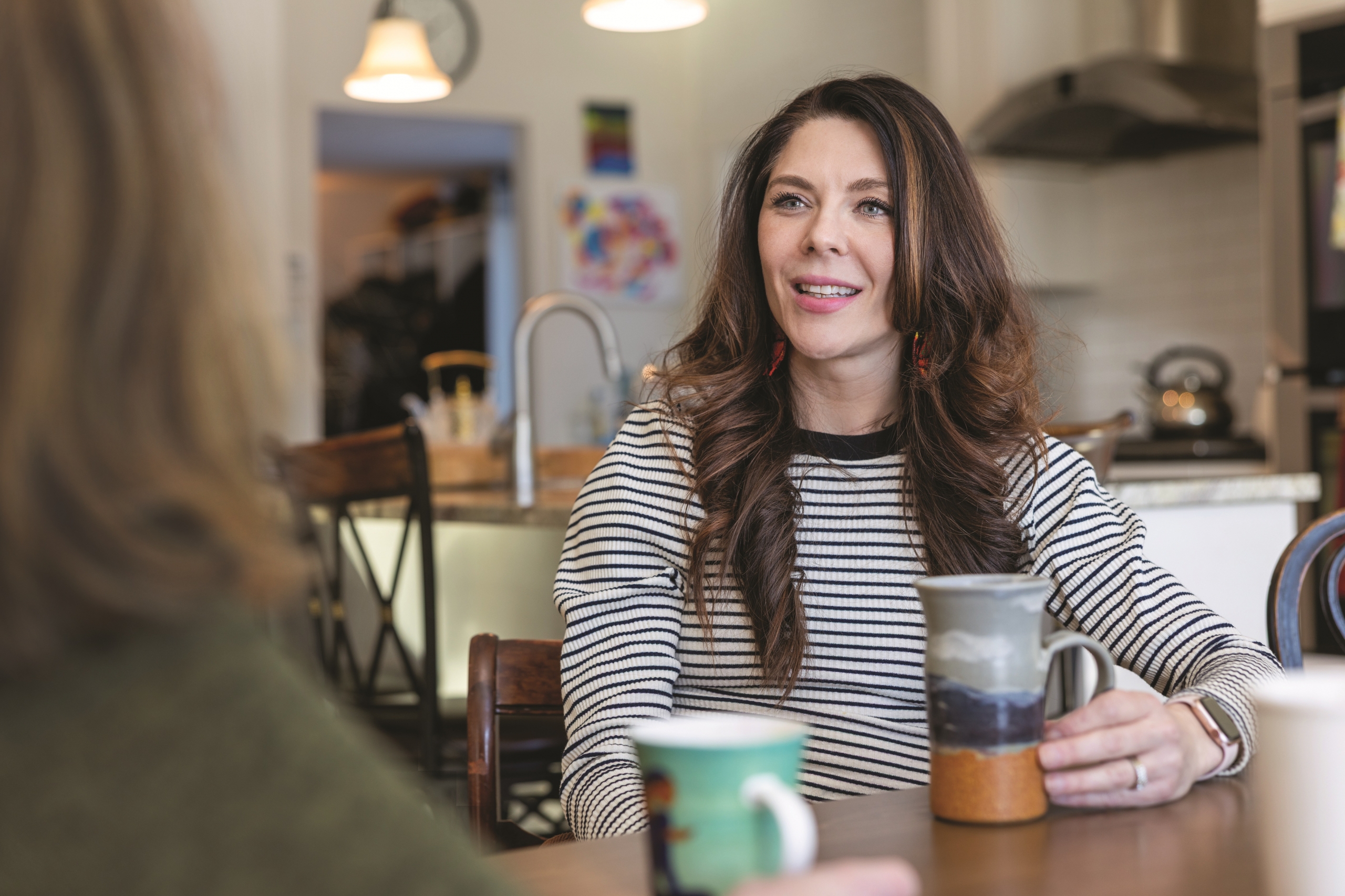 Vanessa Van Bewer speaks with a woman at a kitchen table.