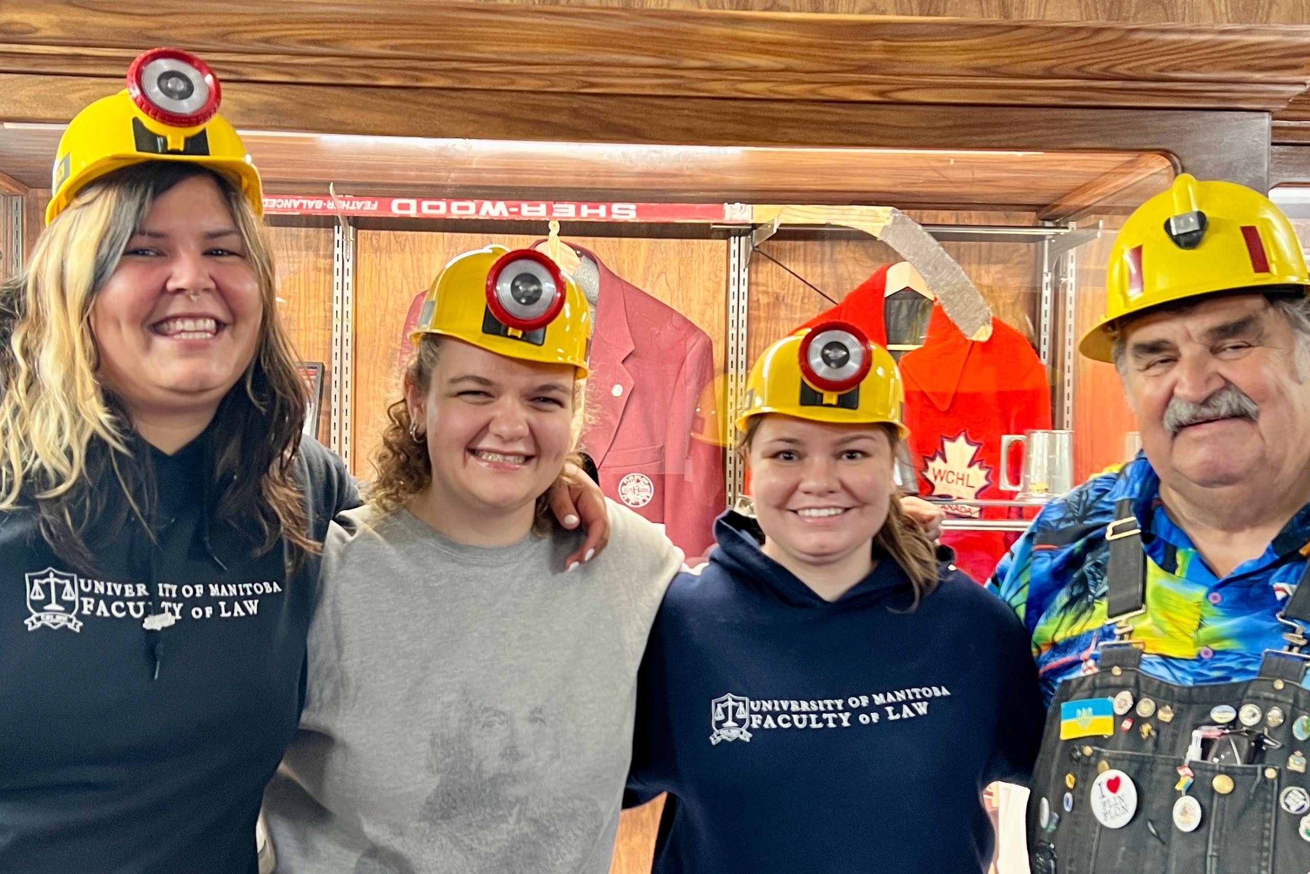 three women and one man in yellow miner hats smile together