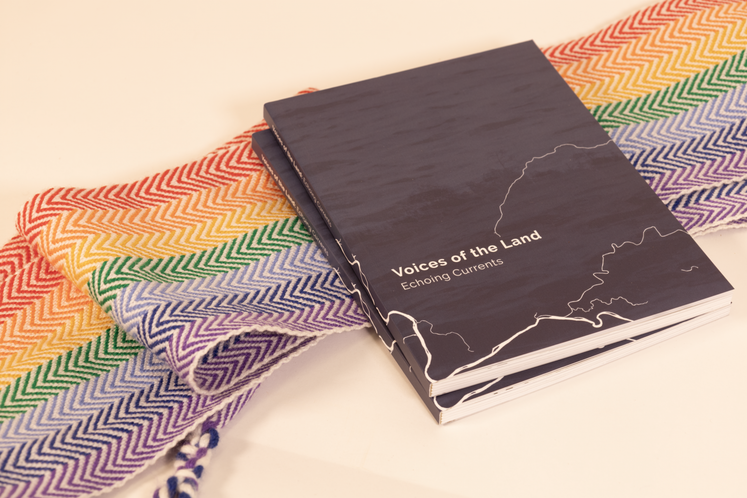 Dark book titled “Voices of the Land: Echium Currents” rests on a colorful woven textile, creating a calm, artistic scene.