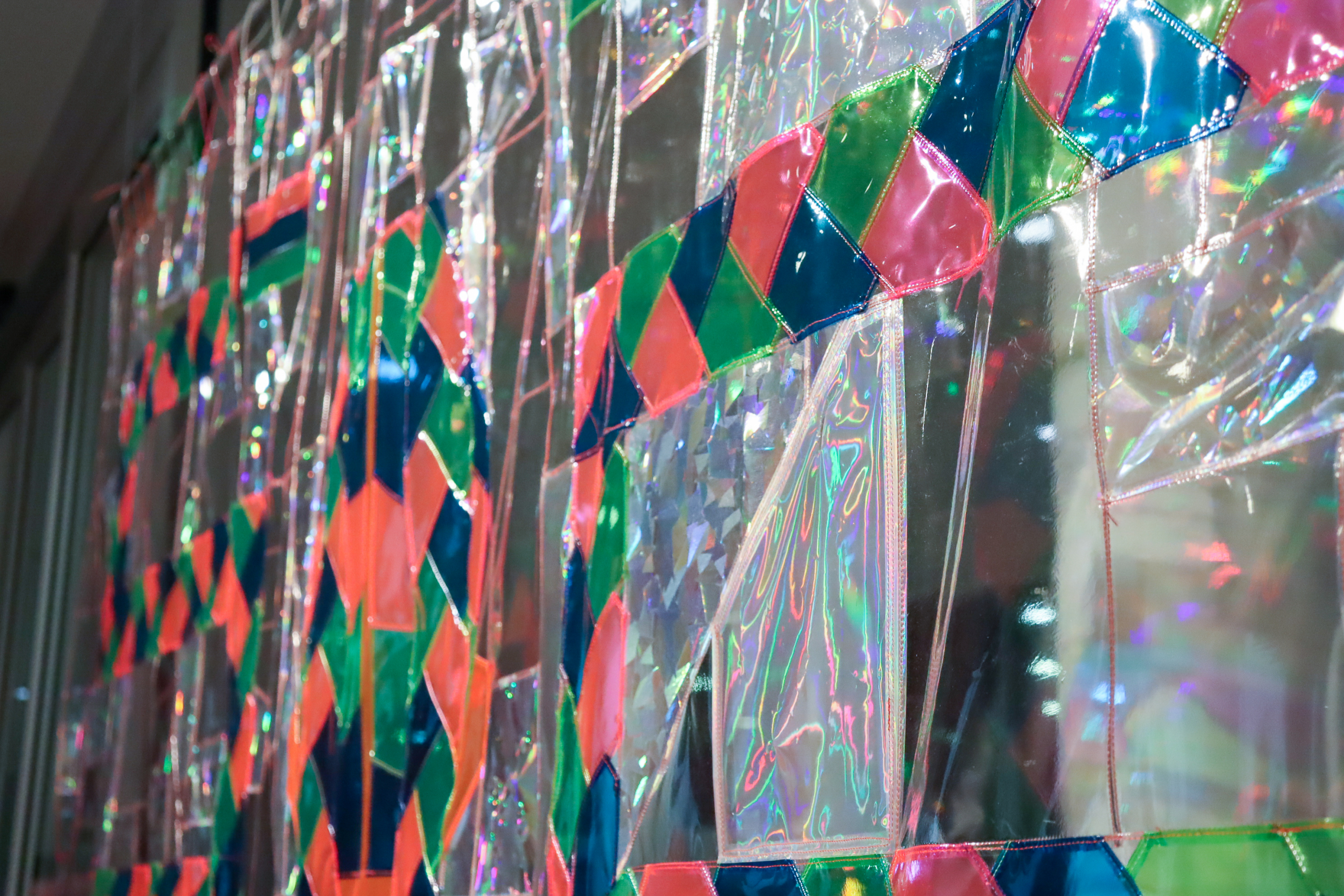 Angled close-up of shimmering plastic and fabric patchwork with a colourful diamond pattern stitched across the surface.