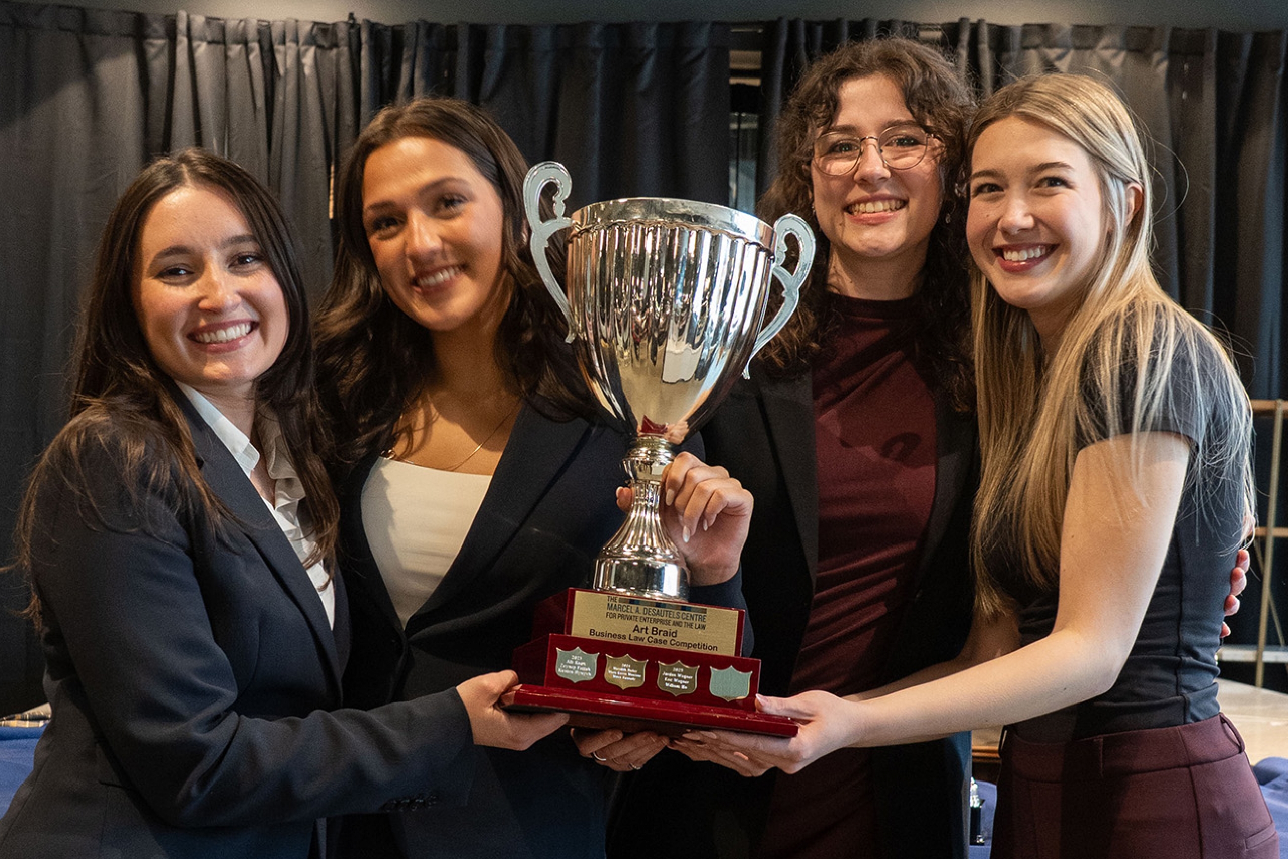four law students in dress clothes hold a large trophy between them