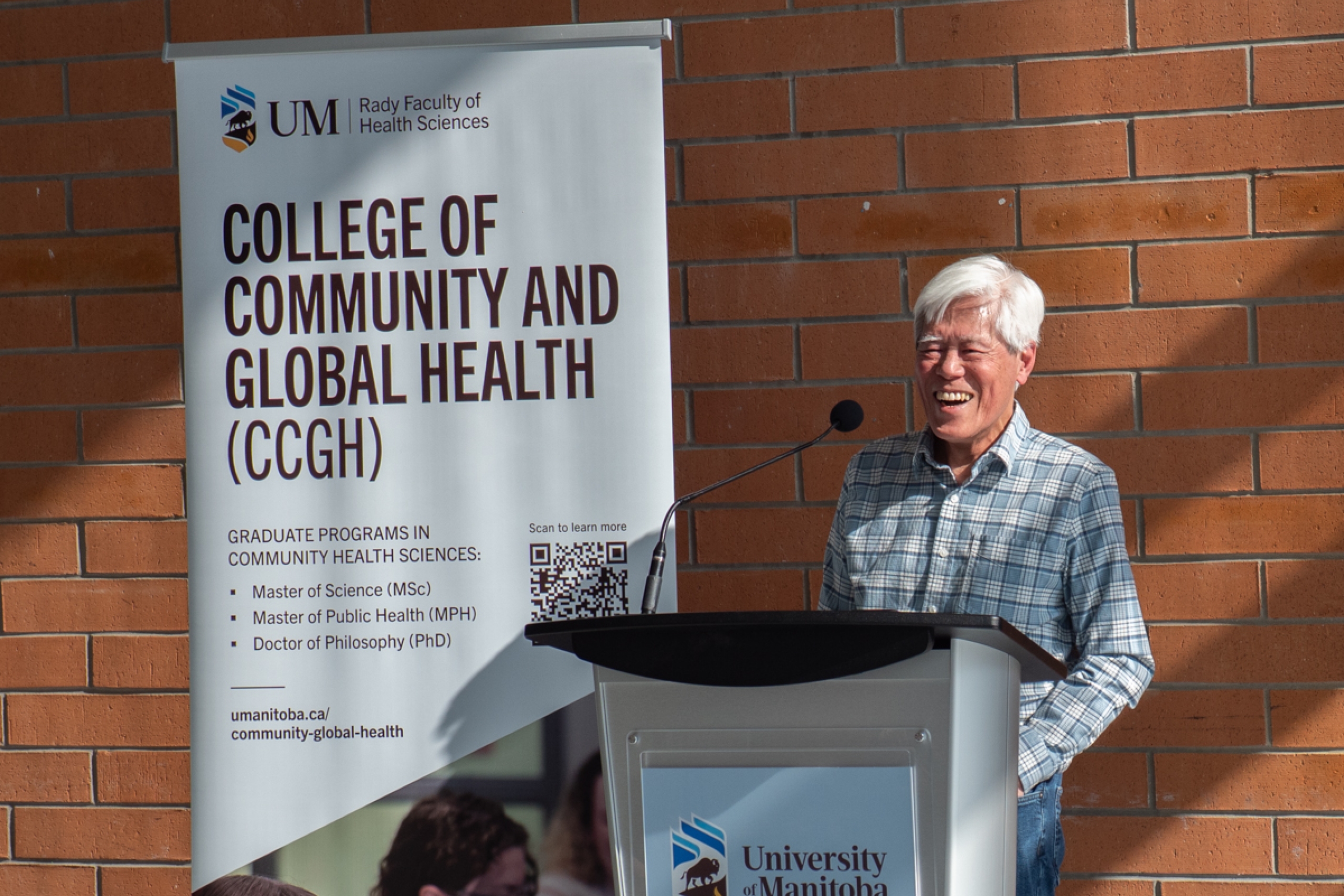 A person stands behind a podium smiling. Beside him is a College of Community and Global Health banner.