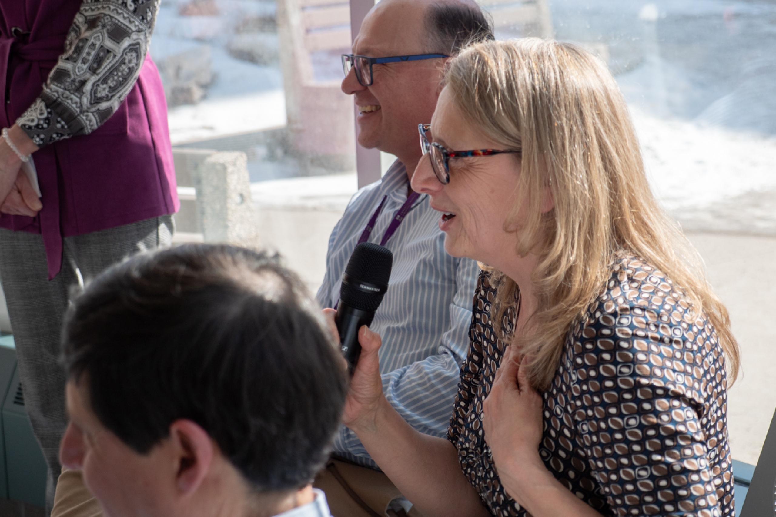 Three people look to the left, the person in the middle is in the middle of talking to a camera.