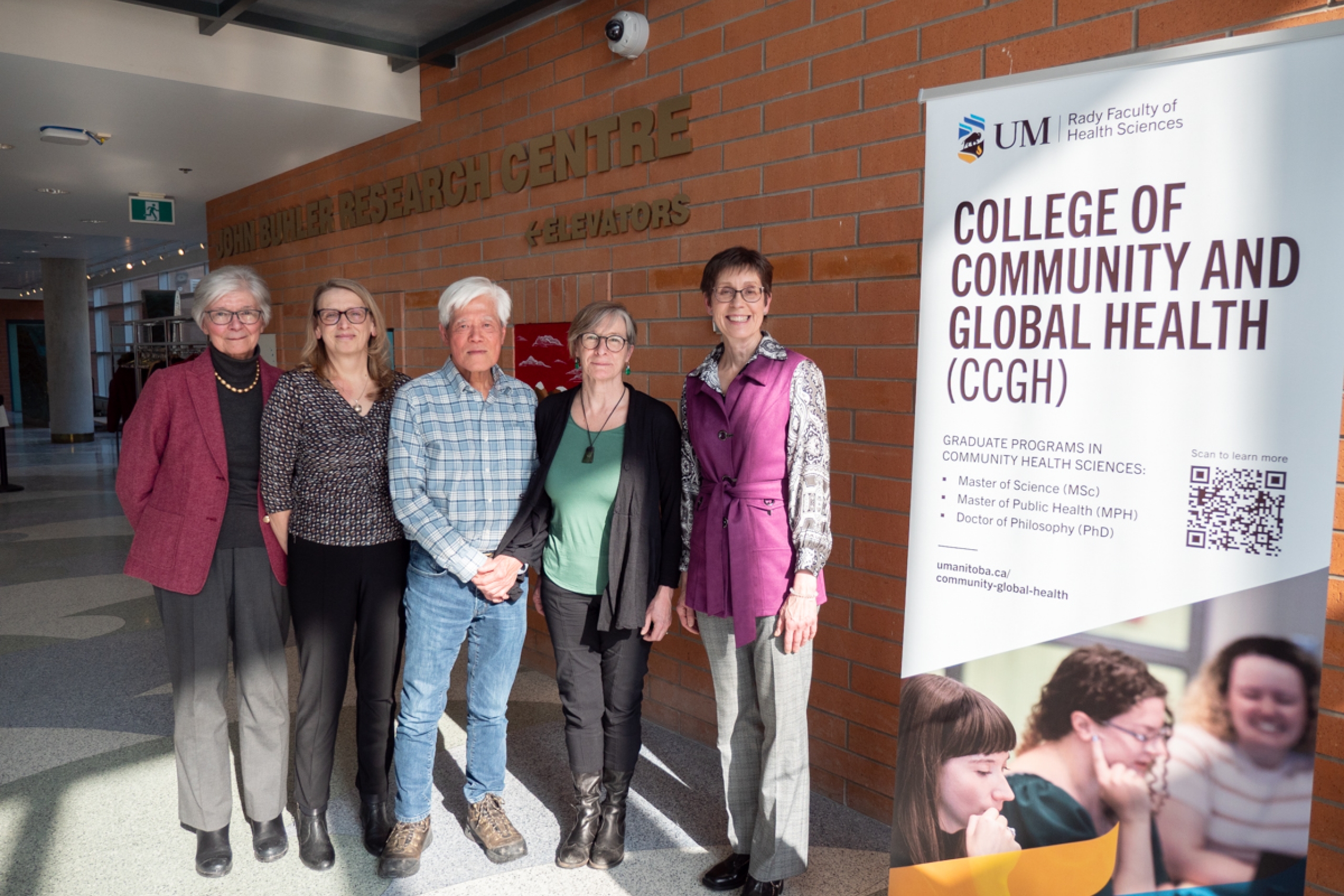 Five people smiles at the camera beside a College of Community and Global Health banner.