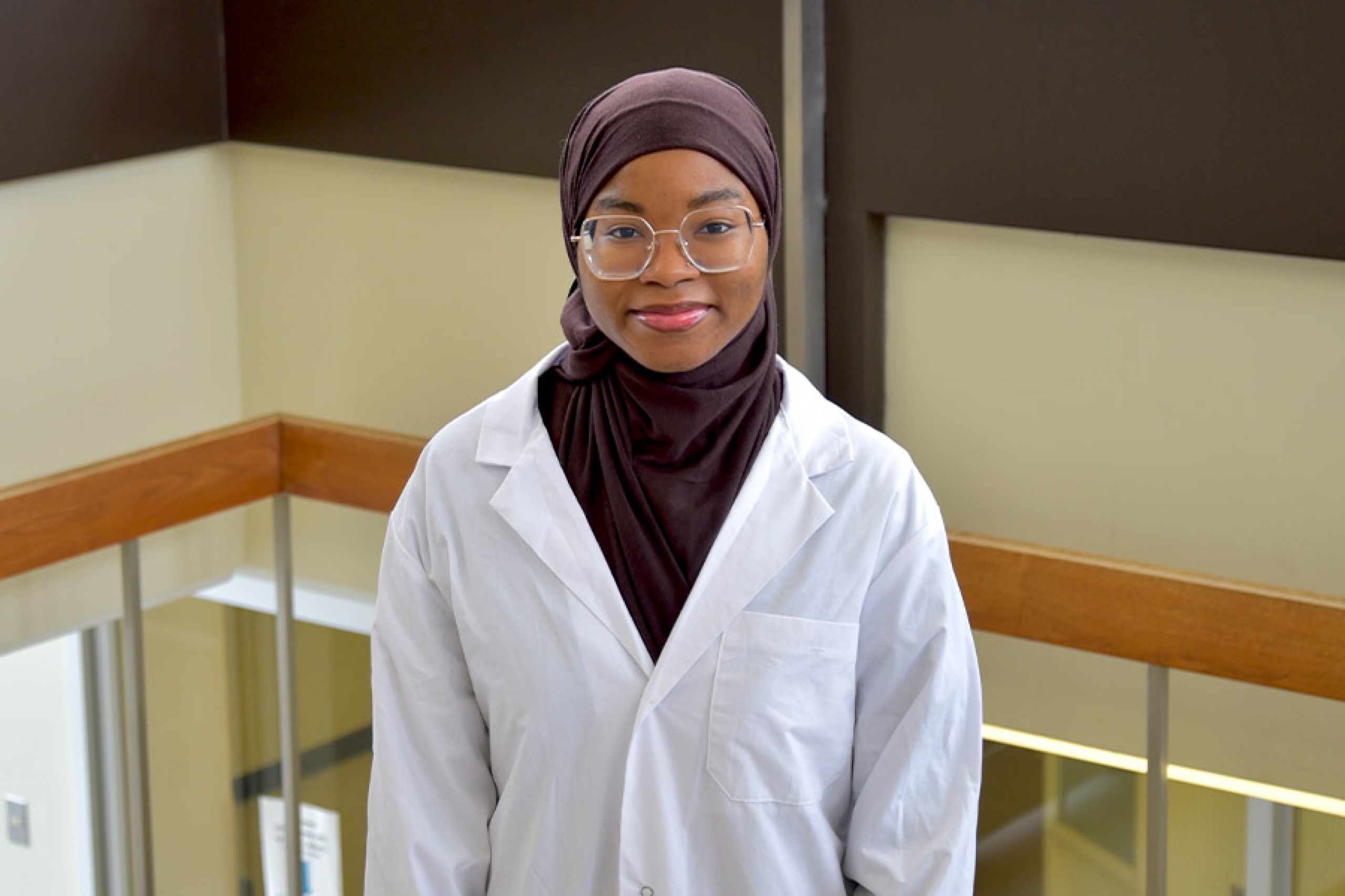 Aliyah wearing a brown hijab and a lab coat smiling at the camera.