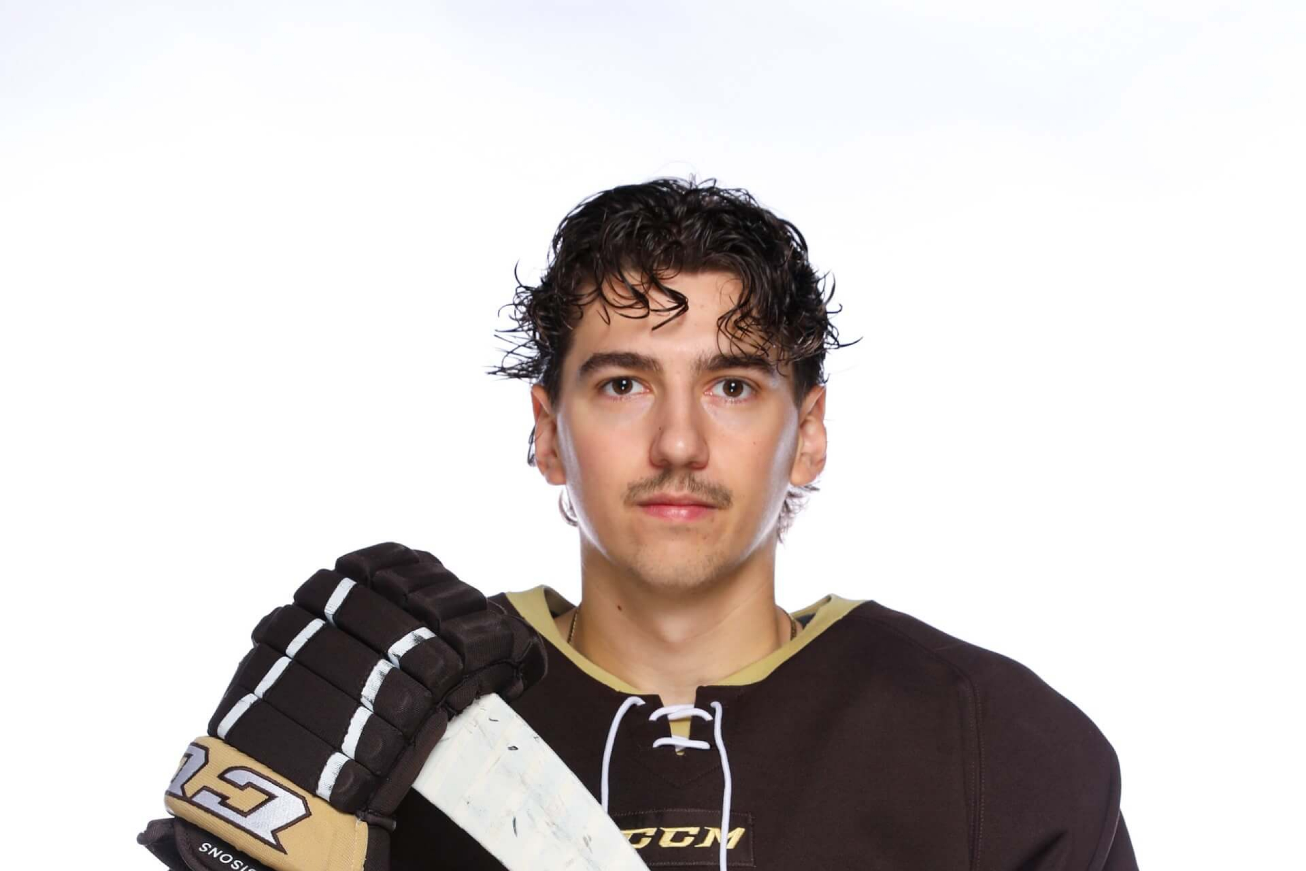 Portrait of Andrew Boucher standing in a black UM Bisons hockey jersey with a hockey stick.