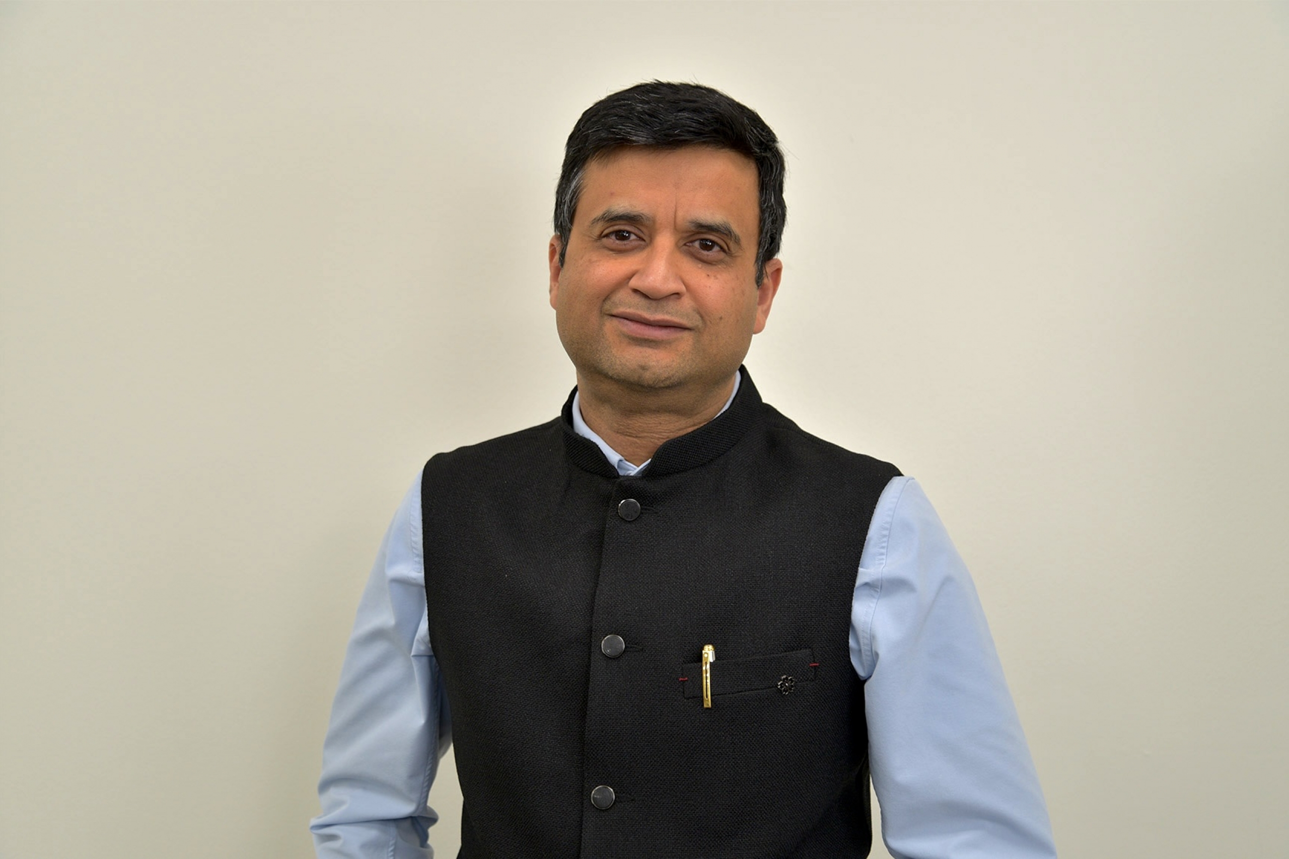 Ayush Kumar wearing a blue long sleeves with a black vest smiling at the camera.