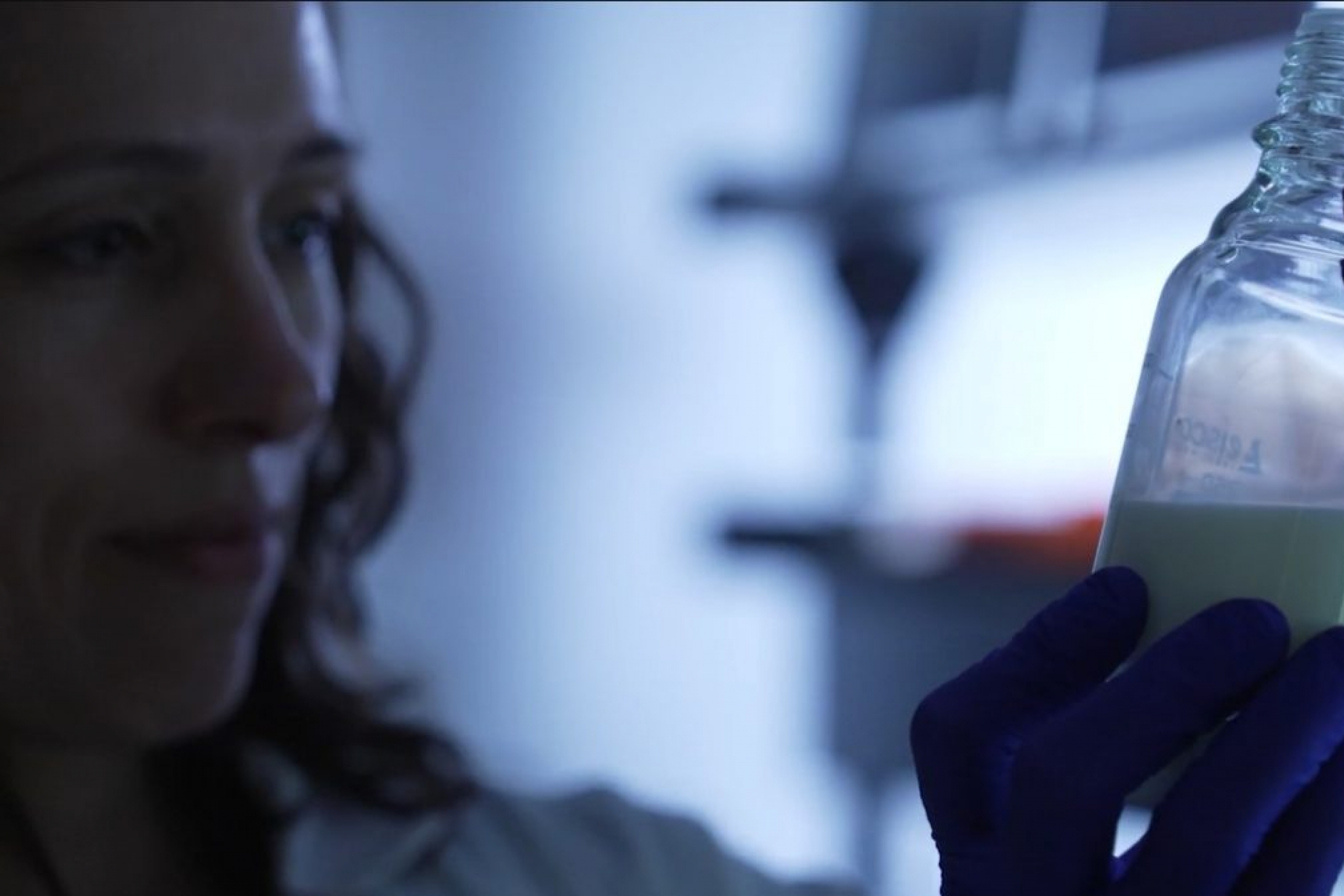A woman holds a bottle in a dimly lit room.