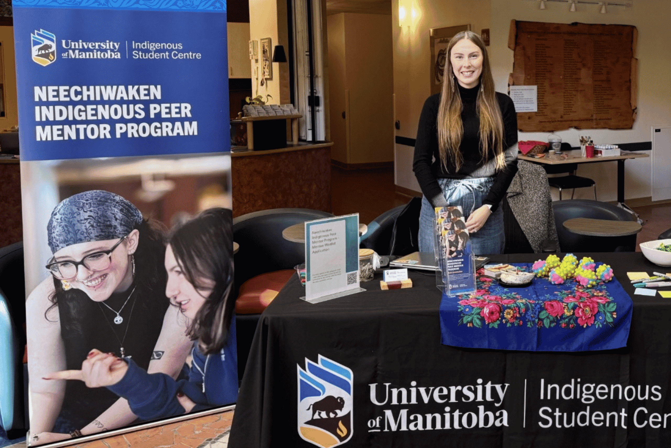 Bailey Pigeau stands behind a Neechiwaken Indigenous Peer Mentor Program display.