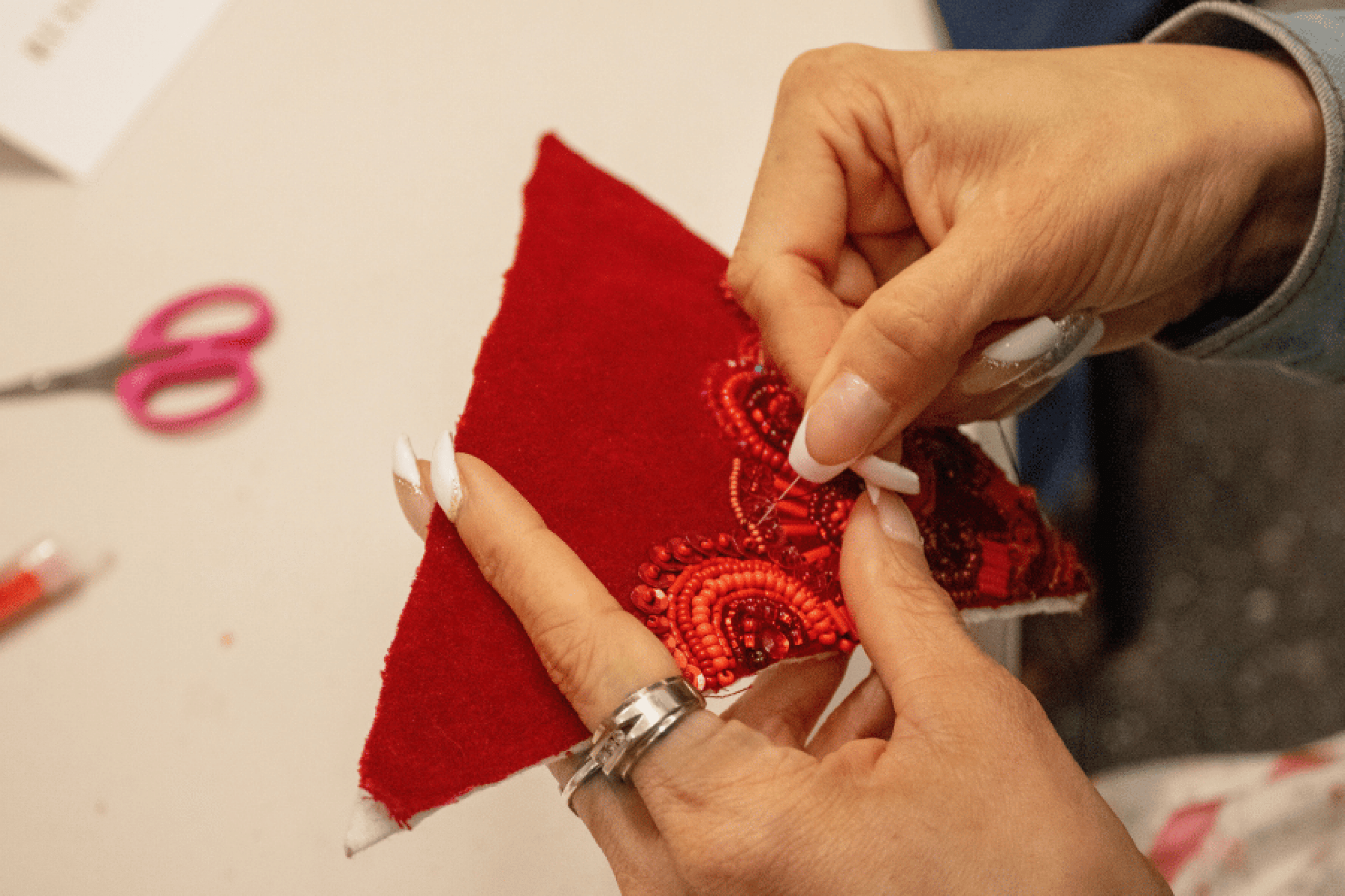 A person stitches red beads in circular patterns onto a piece of red fabric.