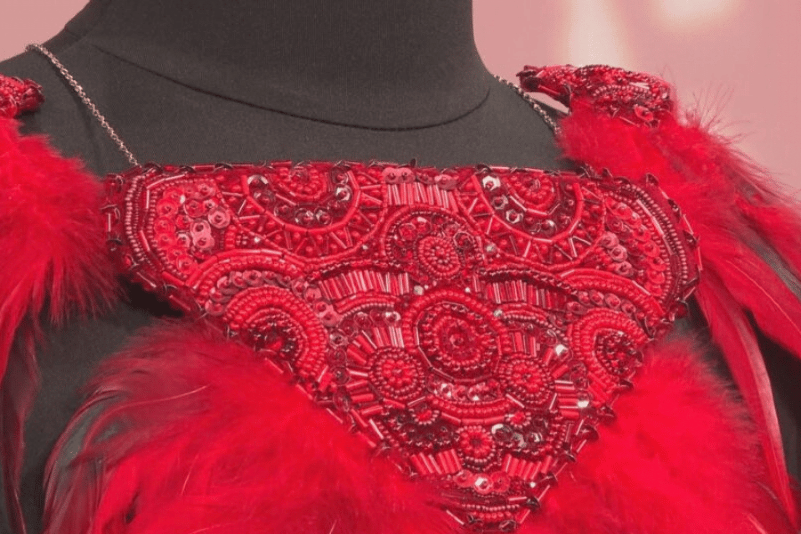 An intricate red beaded collar surrounded by red feathers and displayed on a black dress form.