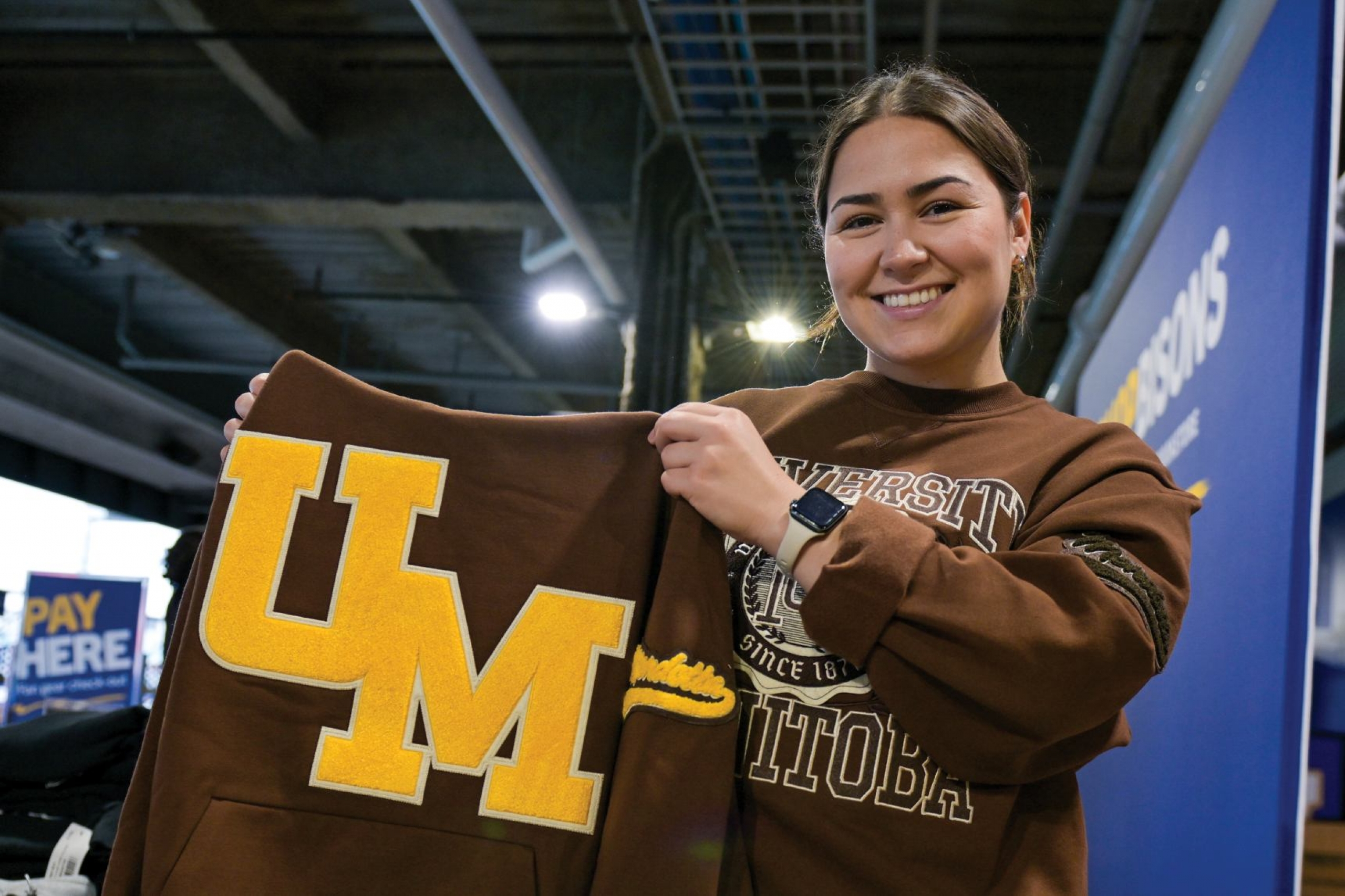 A woman holds a brown sweatshirt with the letters UM embroidered in yellow on it.