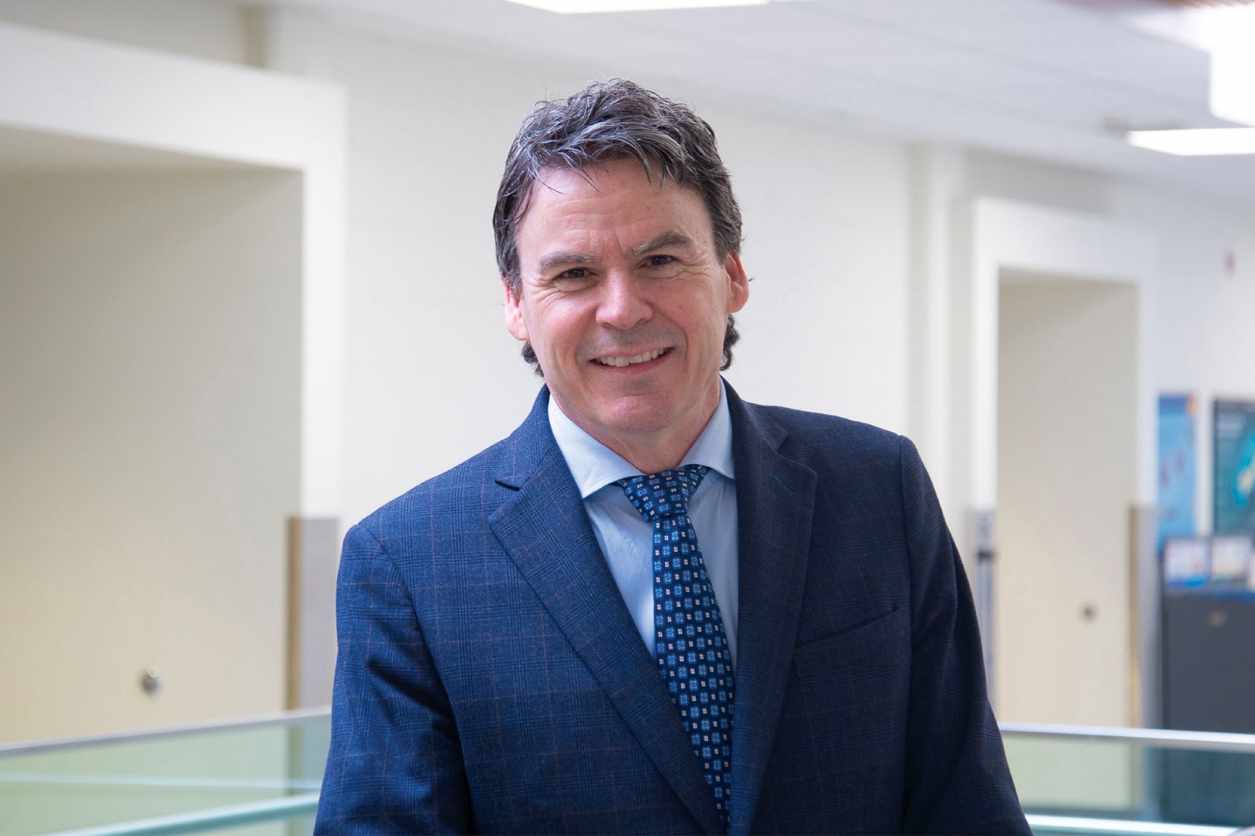 Brian Mark wearing blue tie and blue coat smiling at the camera.