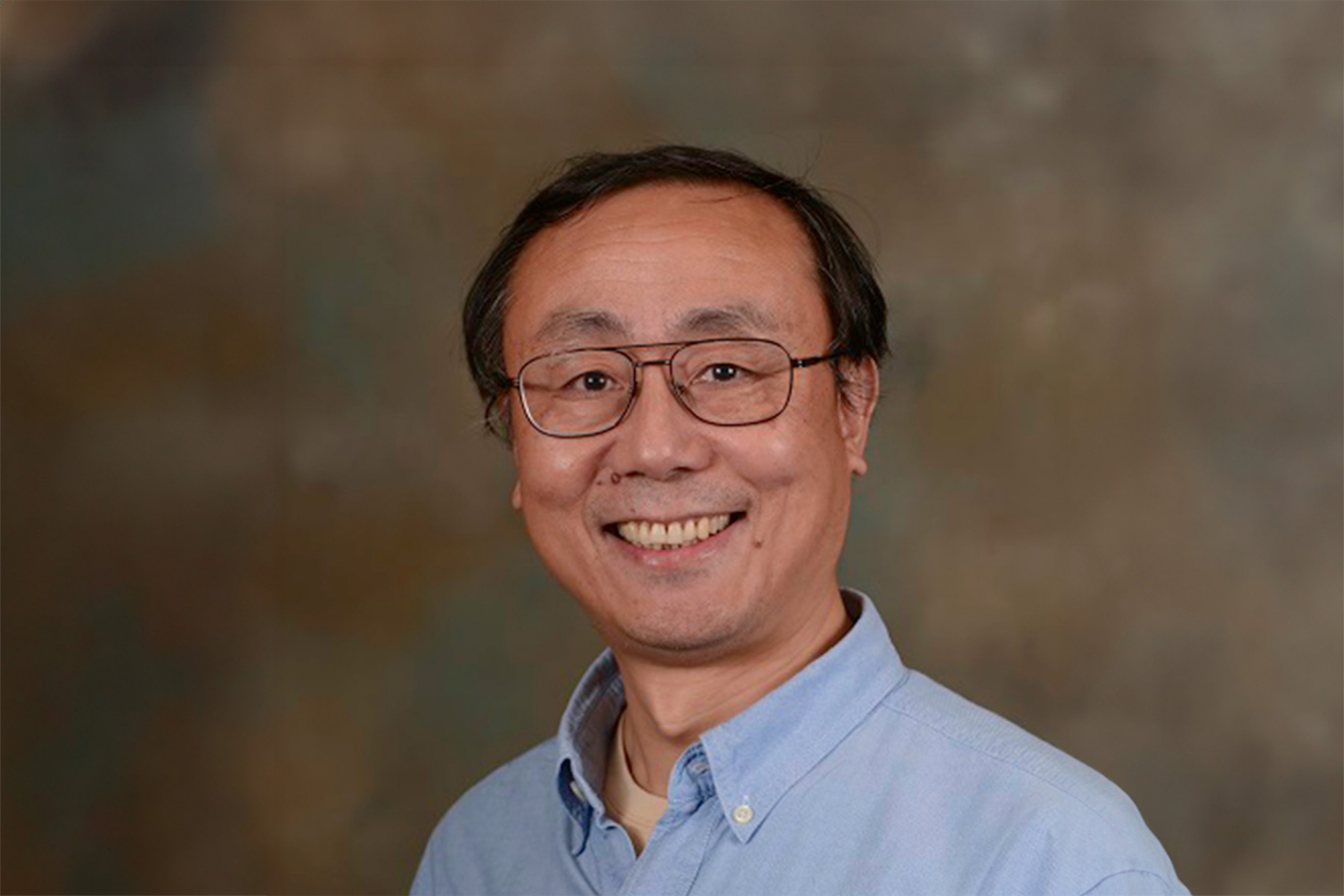 Can Ming-Hu wearing an eyeglass and smiling at the camera.