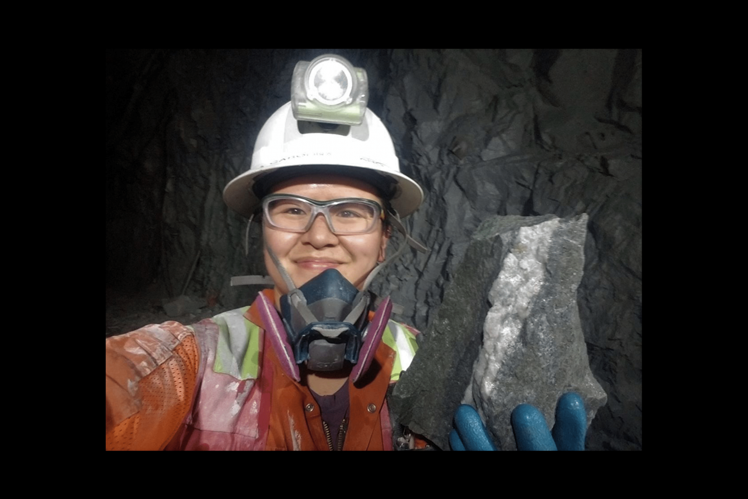 A woman in mining gear including a helmet and headlamp. She is covered in mining dust. 