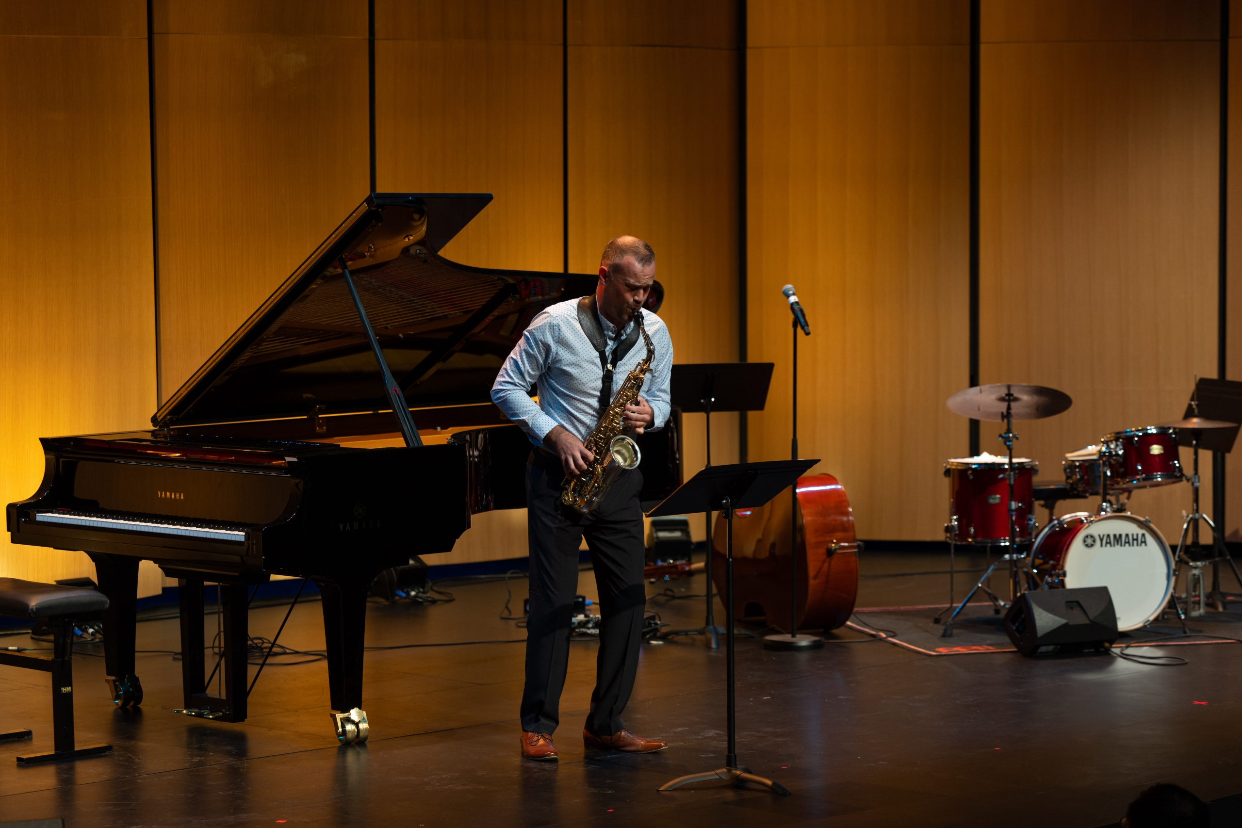 A saxophonist performs onstage with a piano, bass and drum kit.