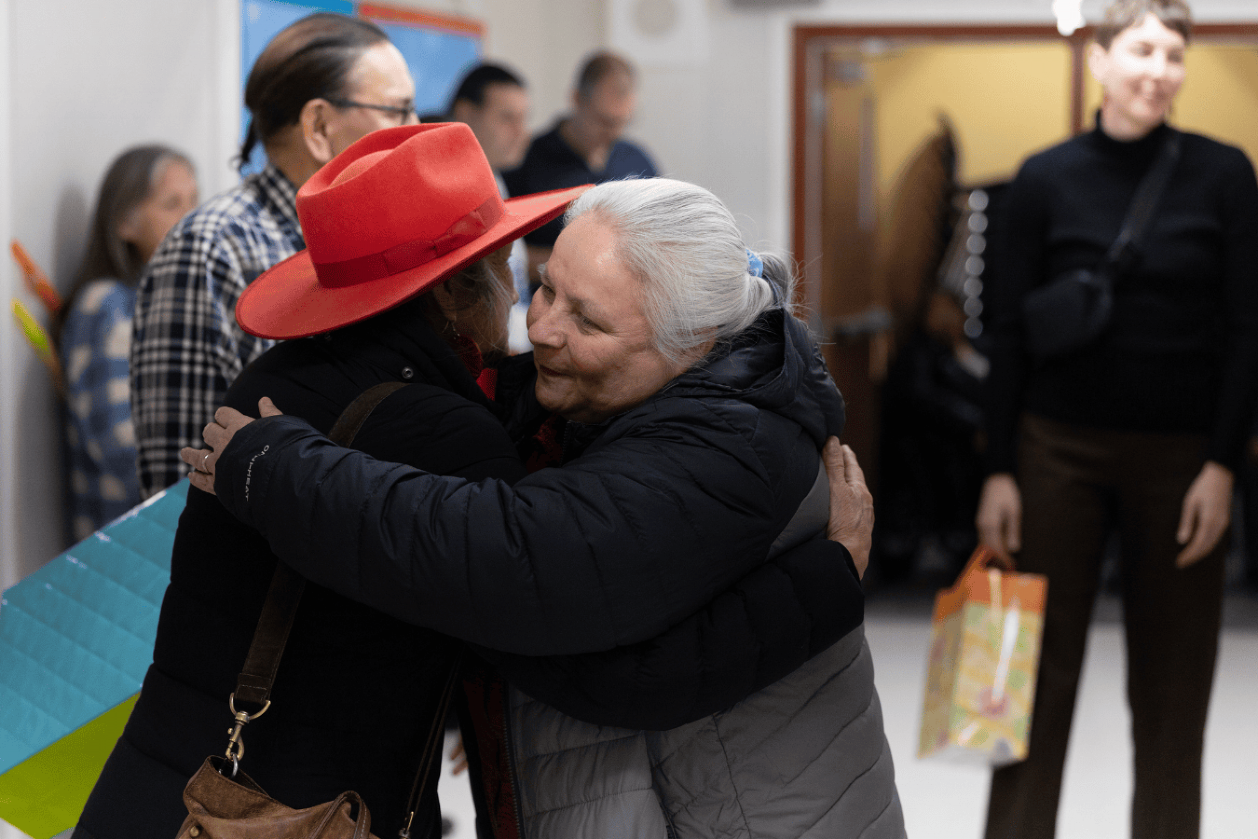 Two people embracing warmly in a school hallway while others stand nearby.