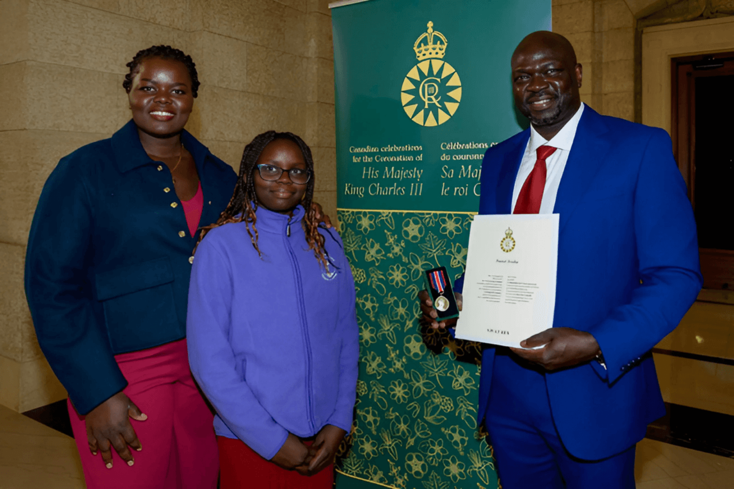 Daniel Swaka holding a paper certificate with wife and daughter.