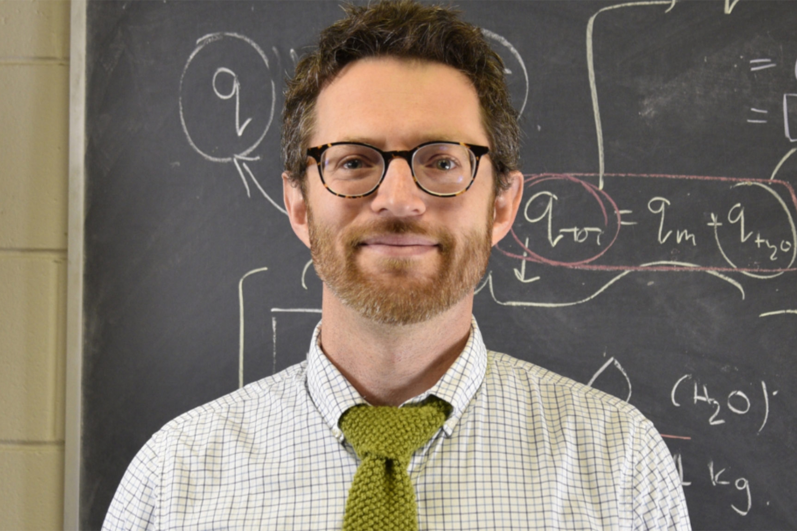 David Herbert wearing a white button down shirt with green tie and an eyeglass smiling at the camera.