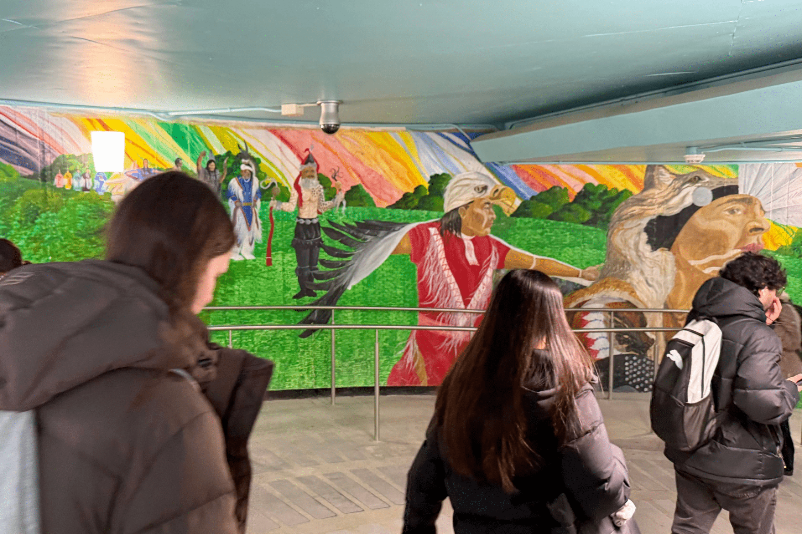 students walking past colourful Indigenous mural in tunnel system on campus.