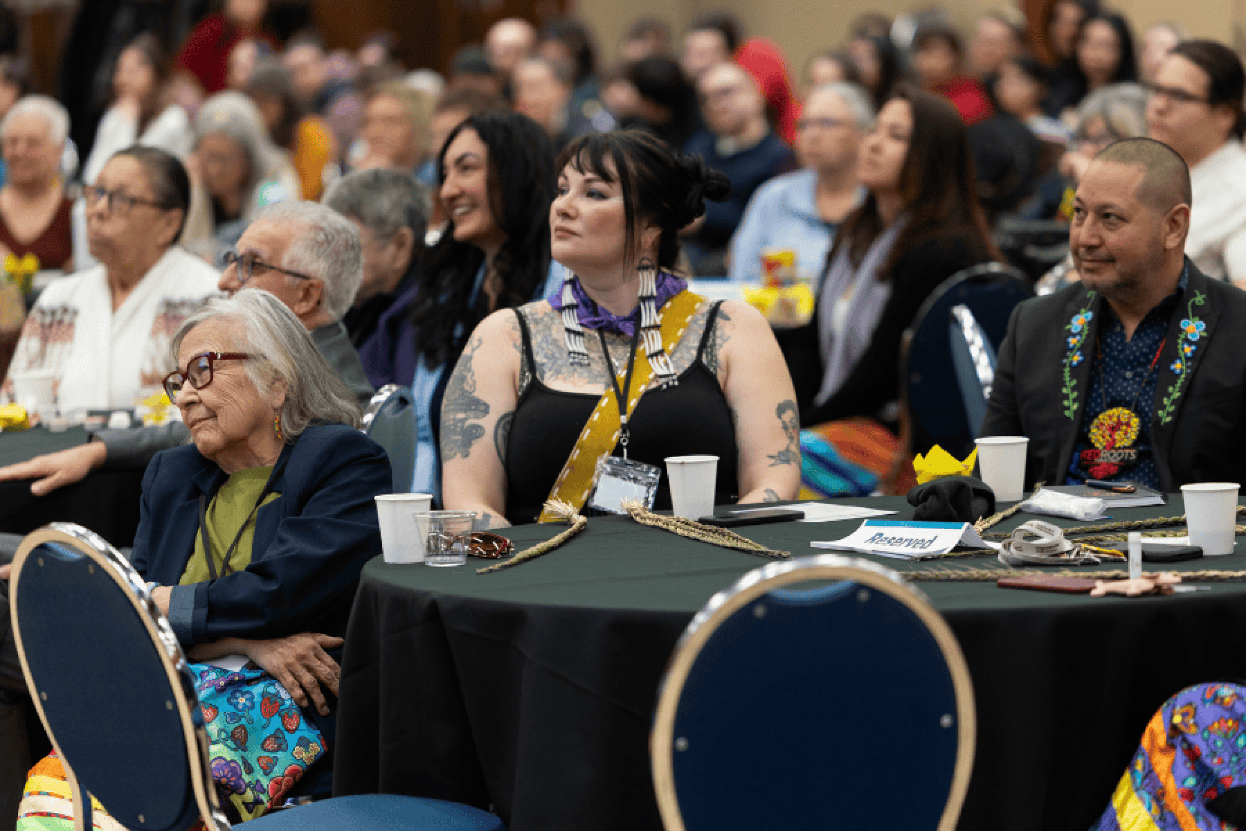 Audience members of different ages sit at round tables, listening attentively during a session at the 2026 Elders and Traditional Peoples Gathering.