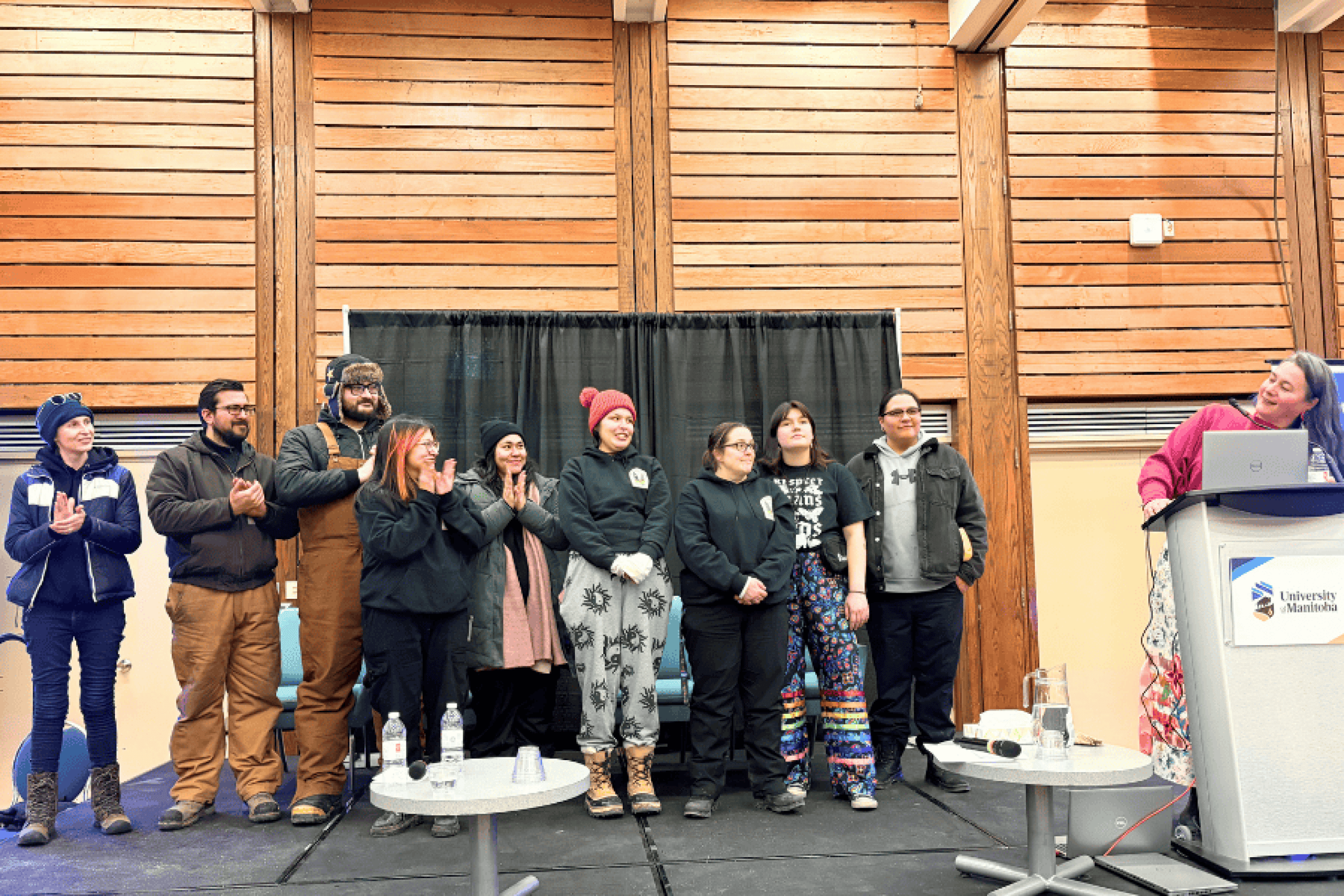 A group of people standing on a stage while others applaud, beside a podium at an indoor event.