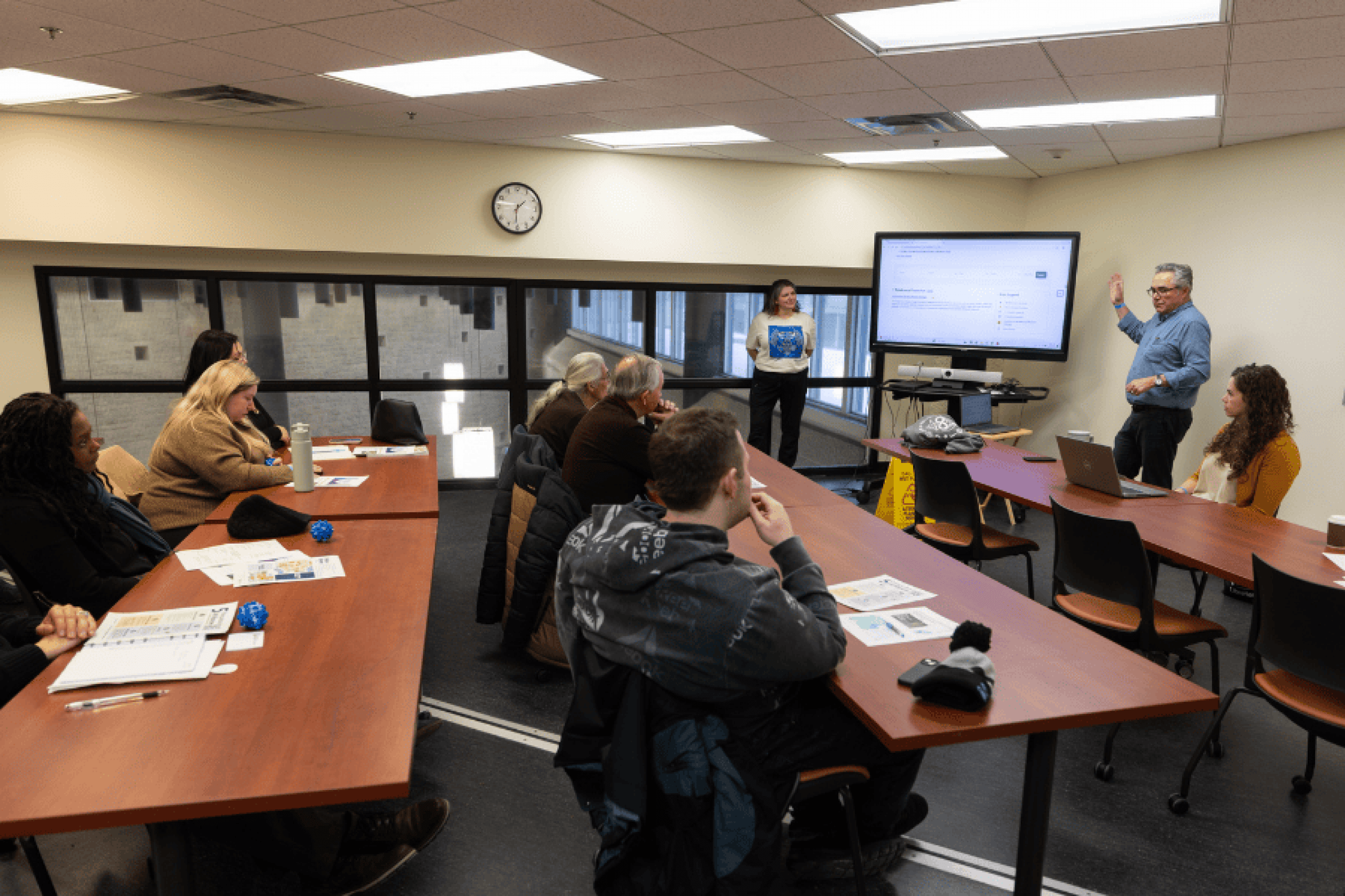 Participants sit at tables during an ETPG session as a presenter speaks beside a screen at the front of the room.