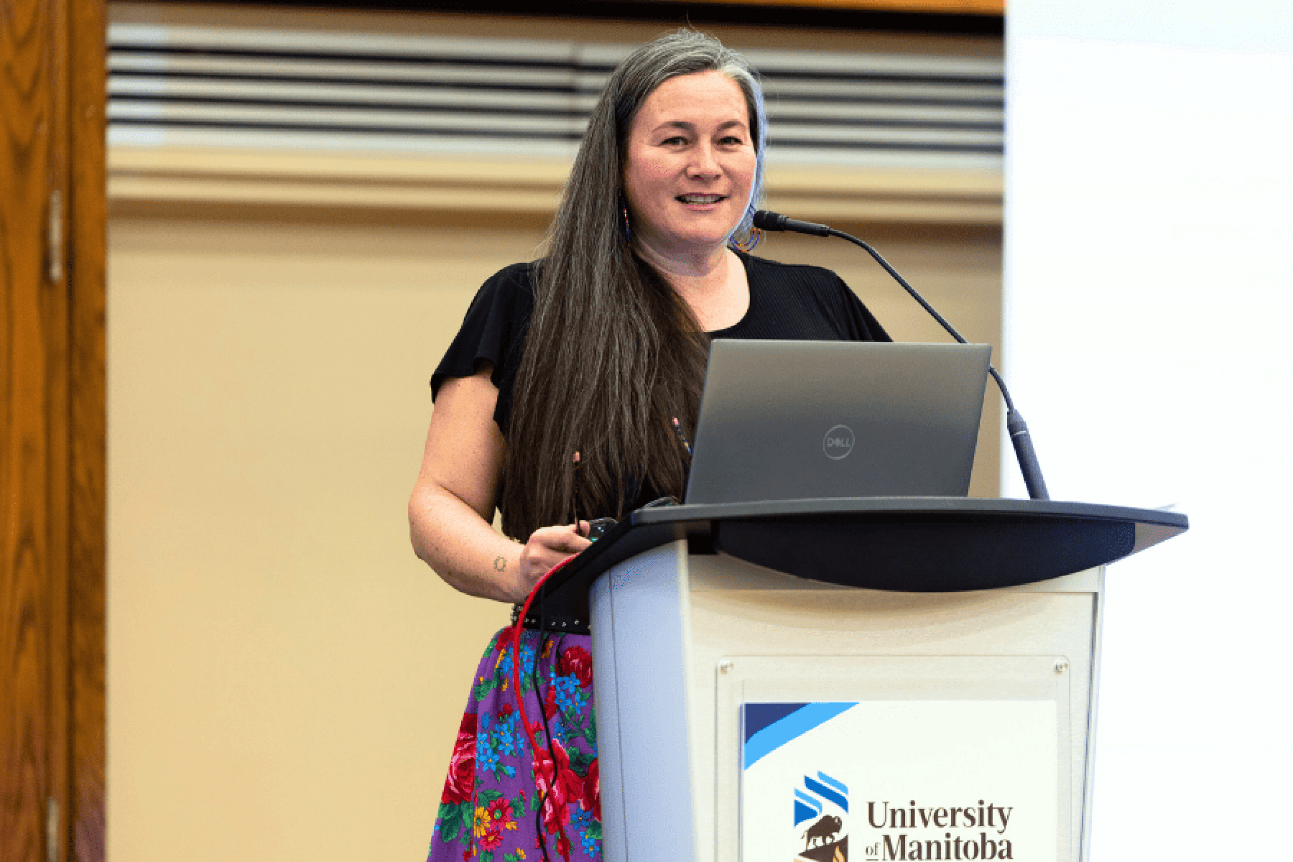 A woman (Vanessa Lillie) speaking at a podium with a microphone and laptop indoors.