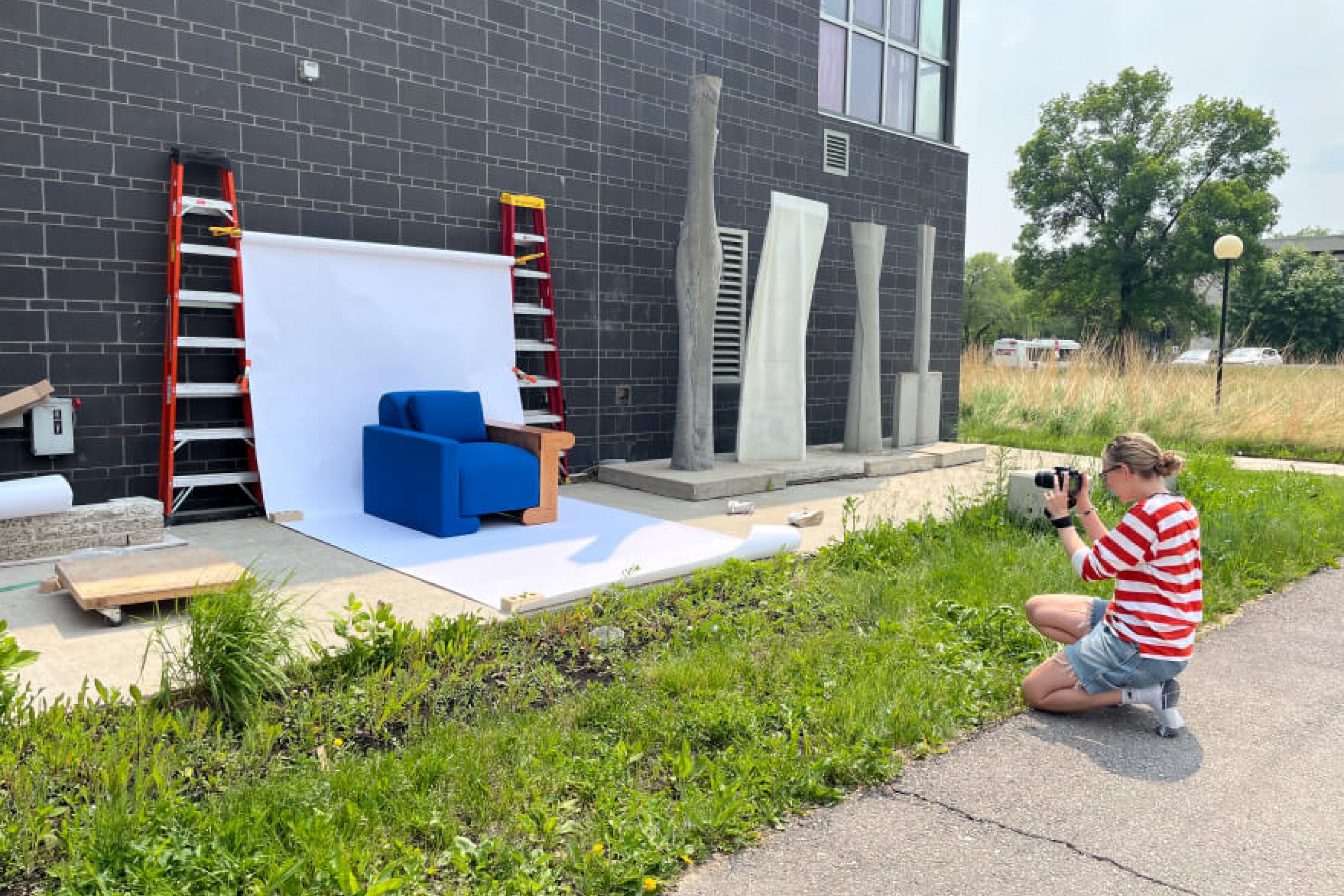 A student taking a photo of a completed, upholstered chair on display in front of a white backdrop.