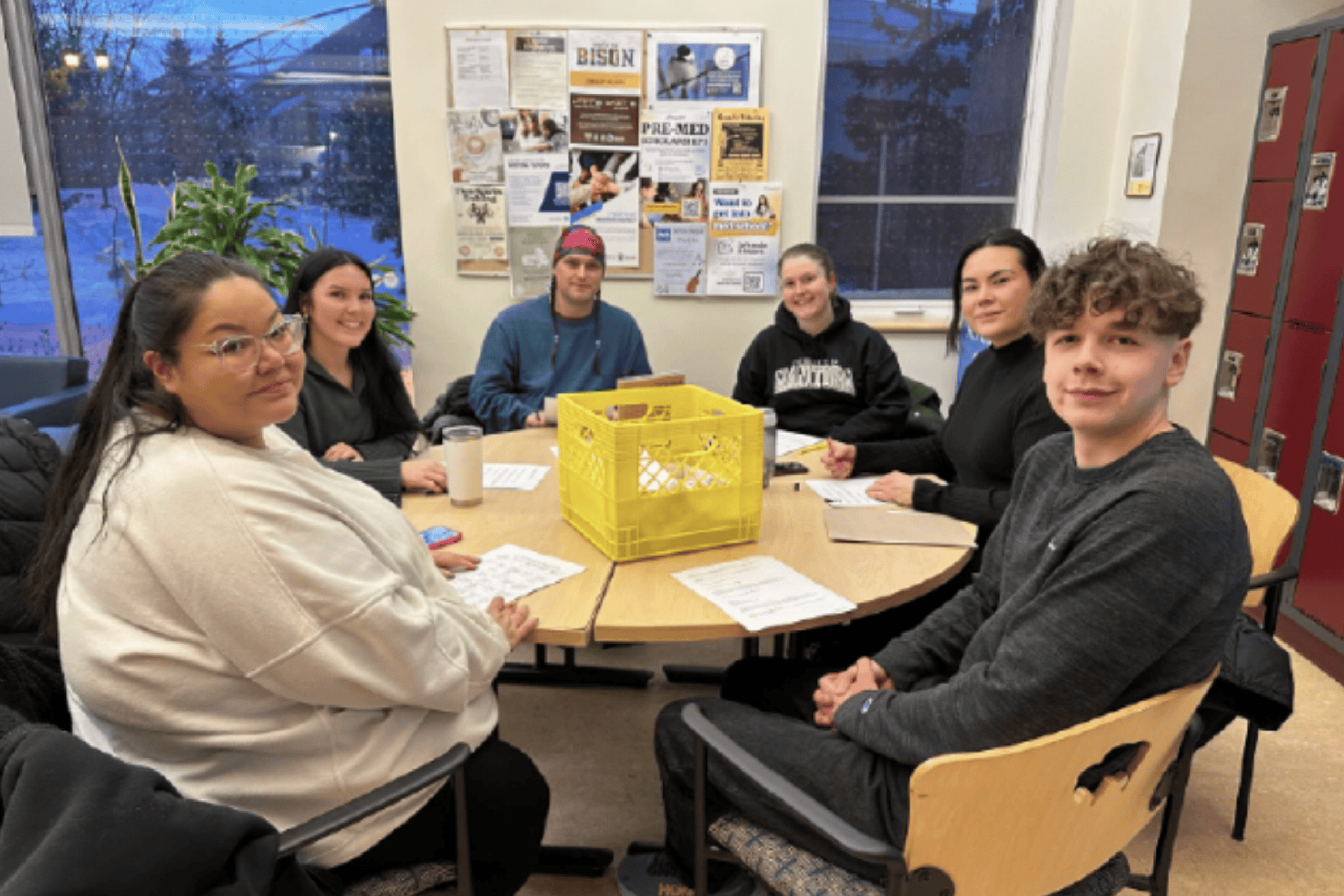 A small group of students sit around a table in a classroom, working together on a project.