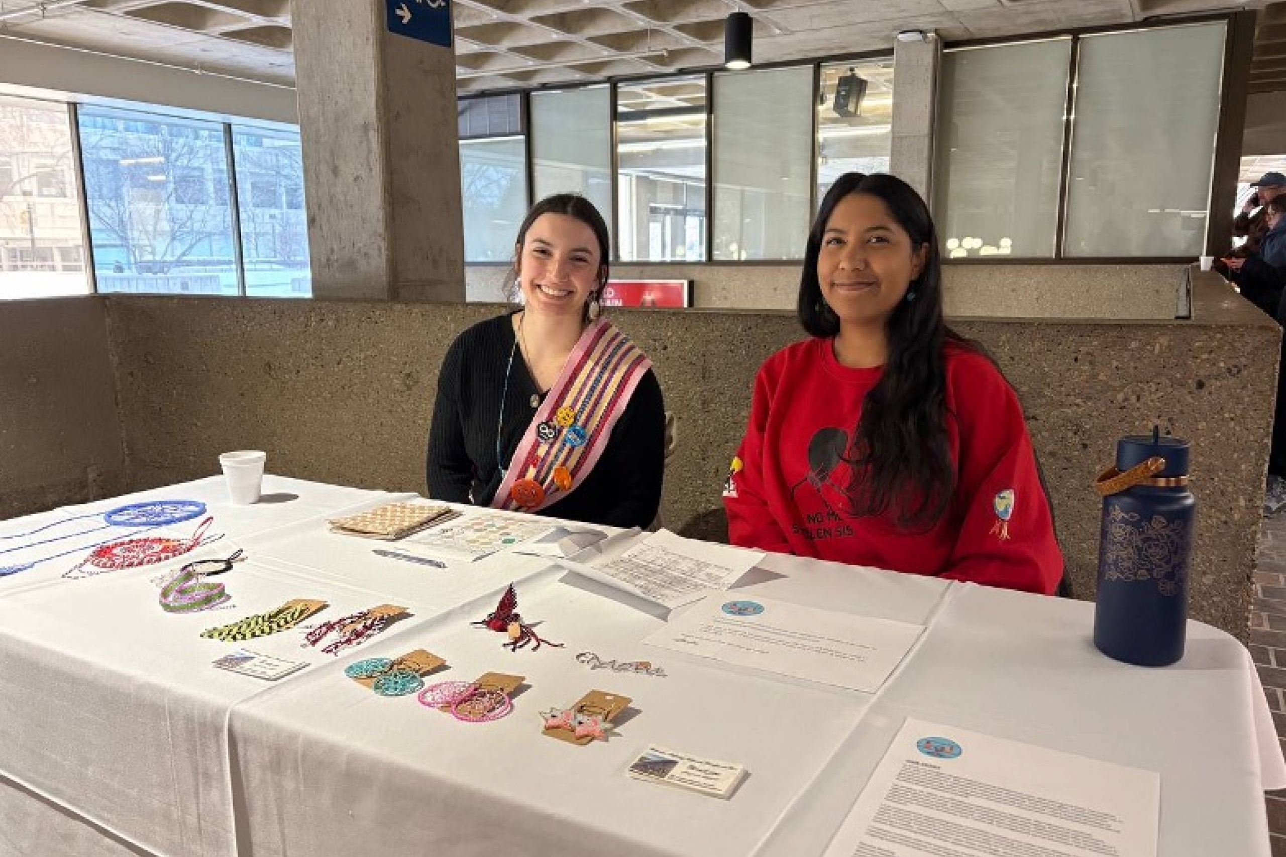 Two students at a table displaying beadwork and informational materials.