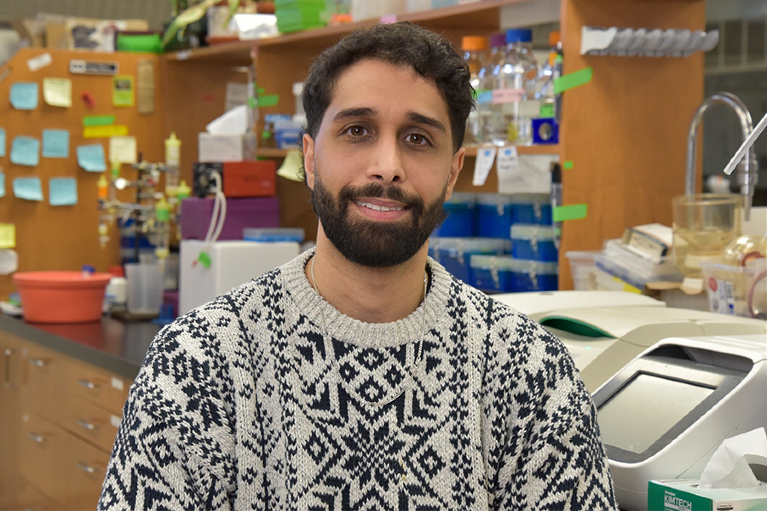 Iman Asakereh wearing a patterned sweater smiling at the camera.