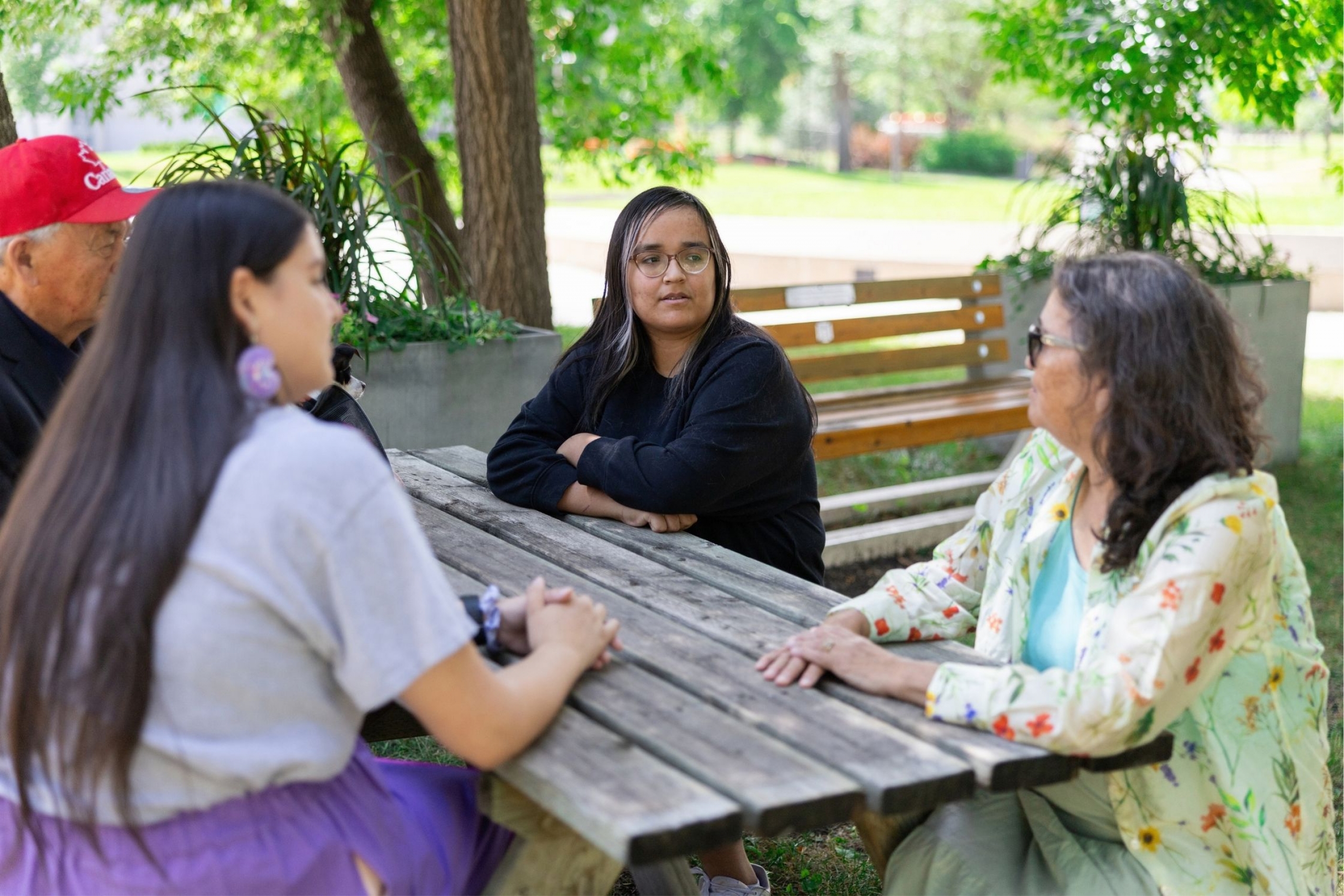Two Indigenous students sit with two Elders outside at a picnic table.
