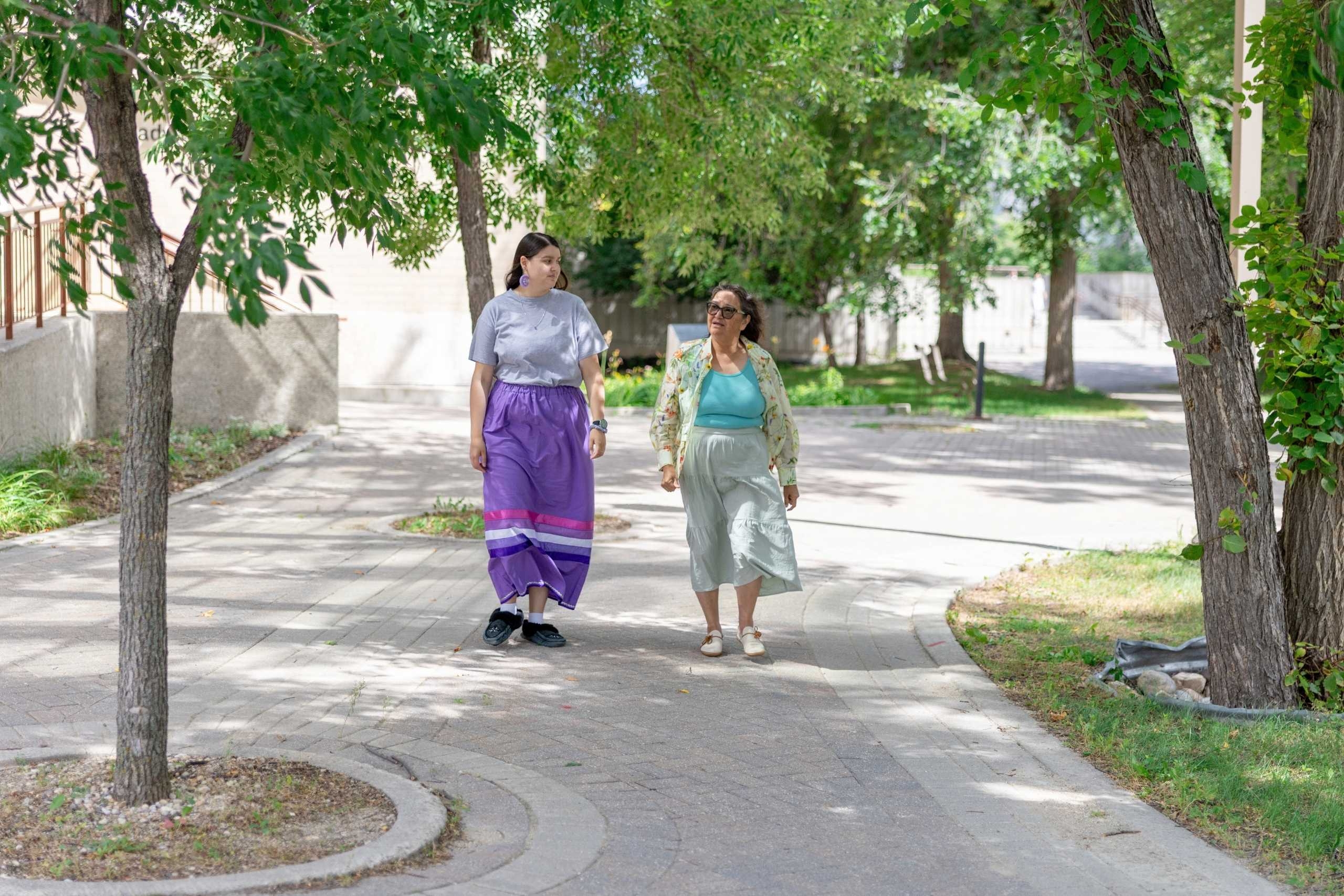 A student and an Elder walk along an outdoor path in the summer.