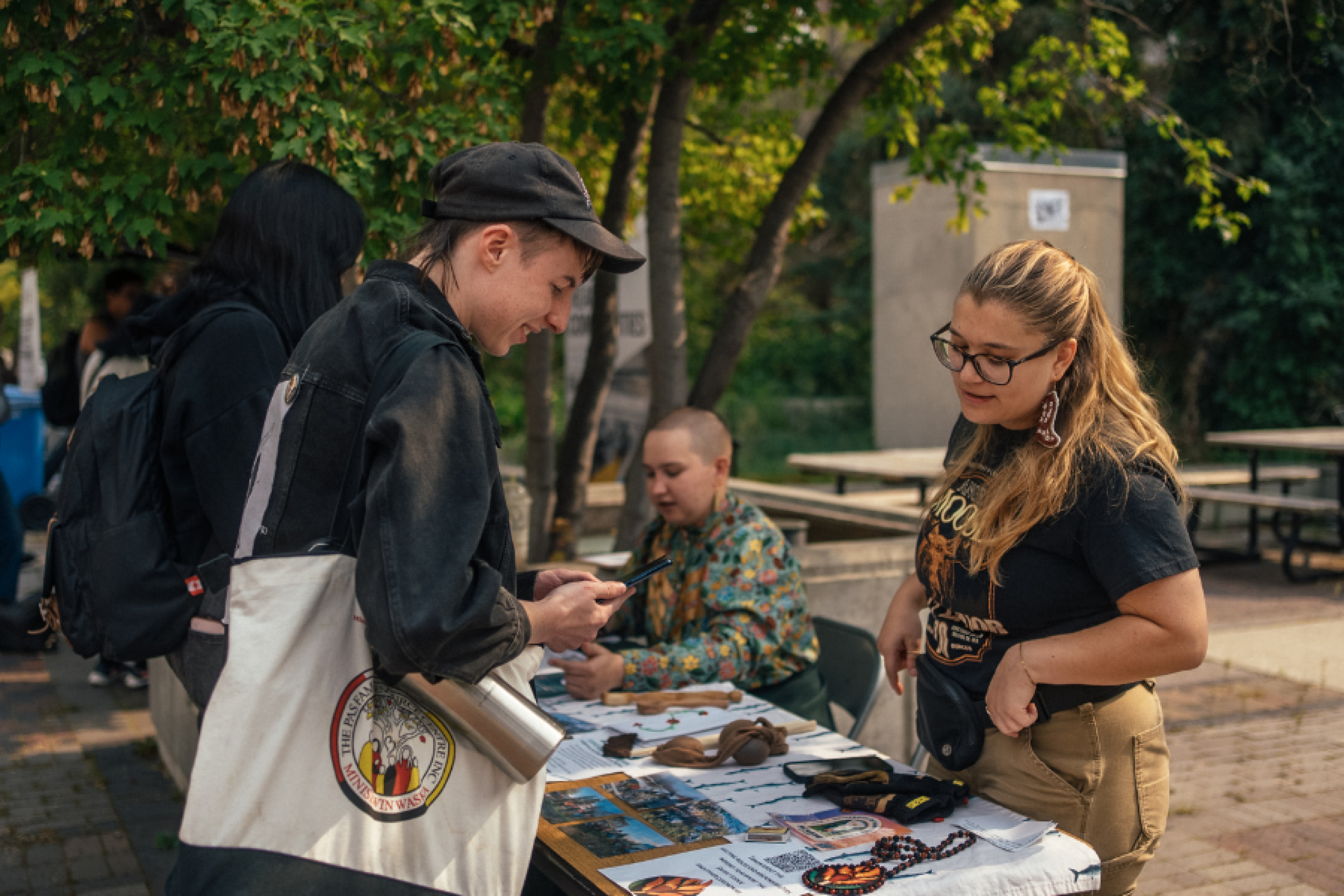 Students engaging at an outdoor information table during a fall campus event, with handmade crafts and pamphlets on display.