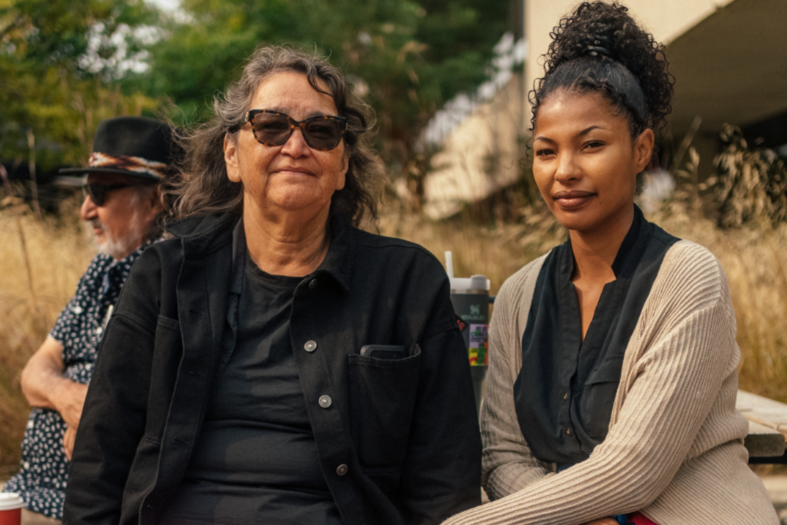 Two women sitting together outdoors during a community gathering, sharing a quiet moment in the autumn sunlight.