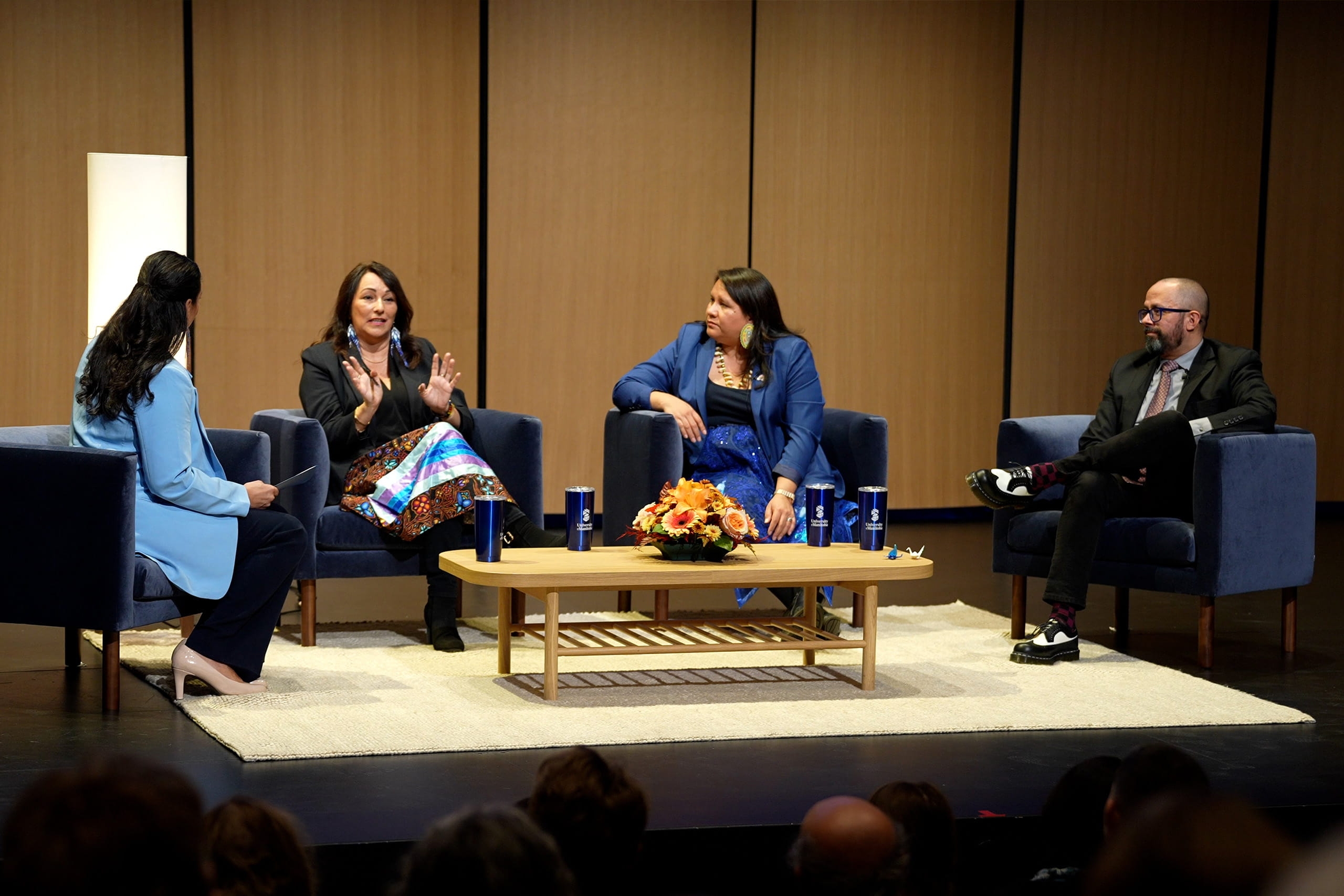 Angie Bruce, Diane Roussin, Kathleen Bluesky and Peter Pomart in conversation seated in chairs on a stage around a coffee table.