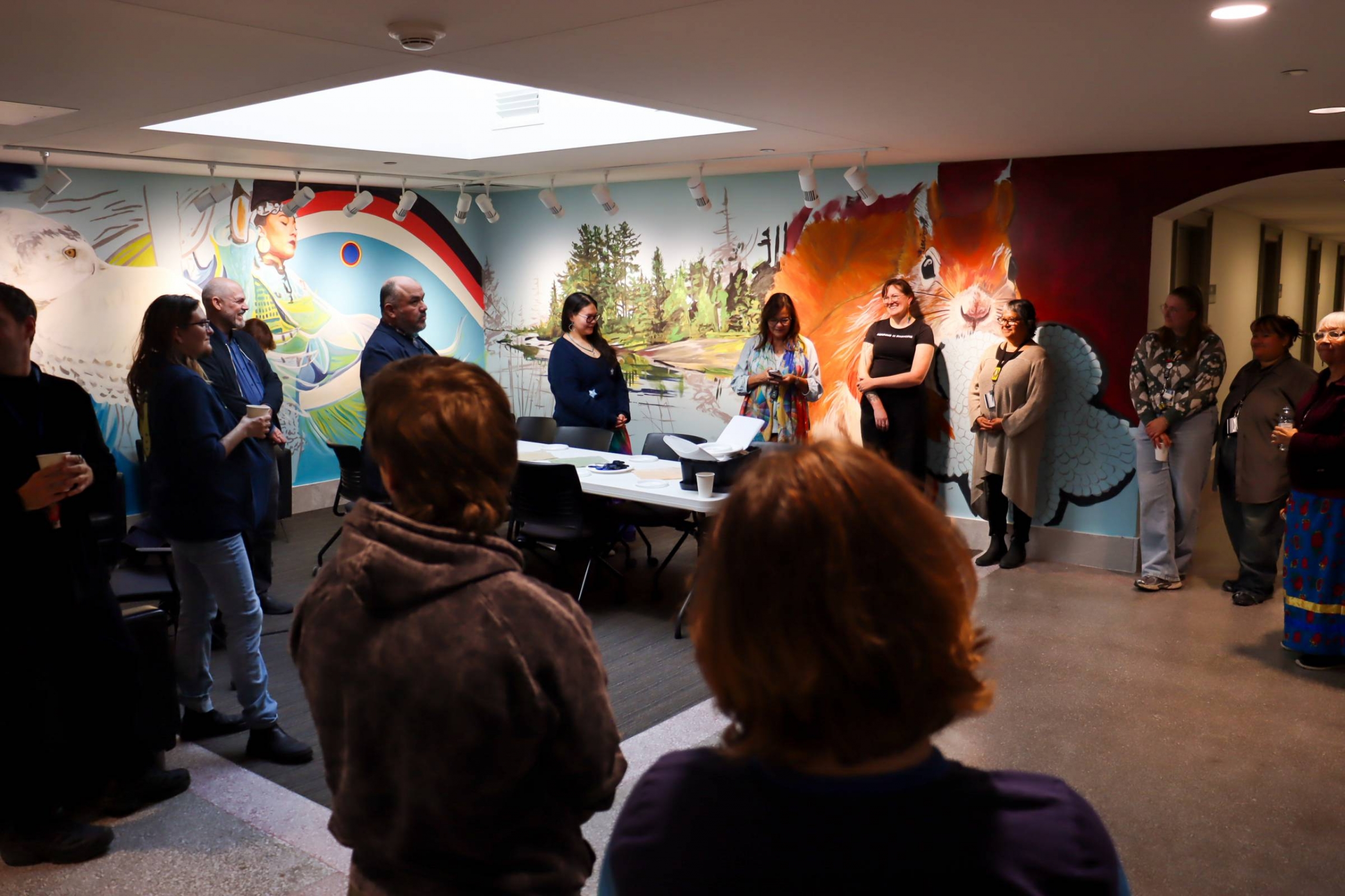 Group gathered in the Indigenous Student Space, standing around a table beneath a colourful mural during opening remarks.