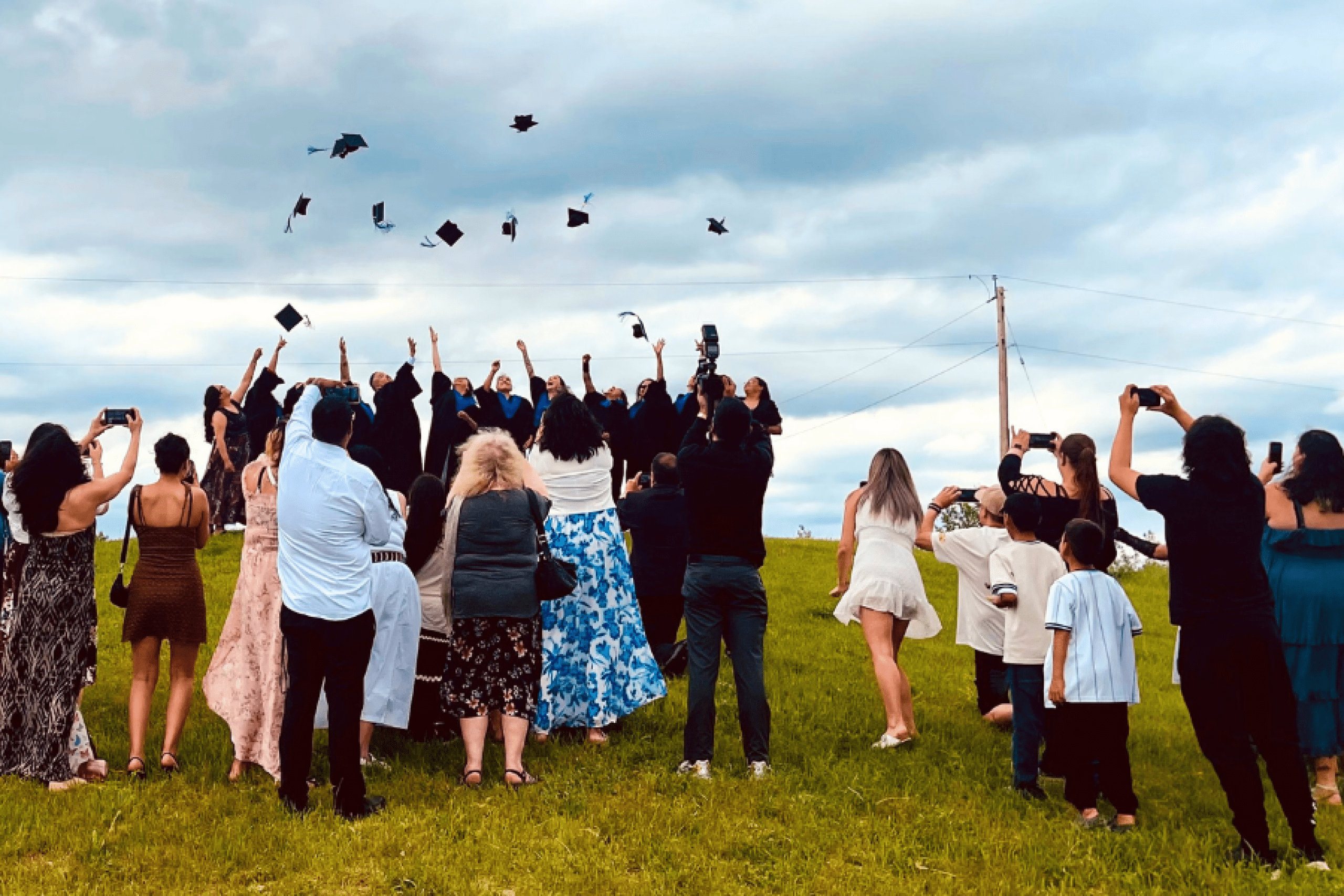 Graduates toss their caps as family and friends celebrate outdoors.