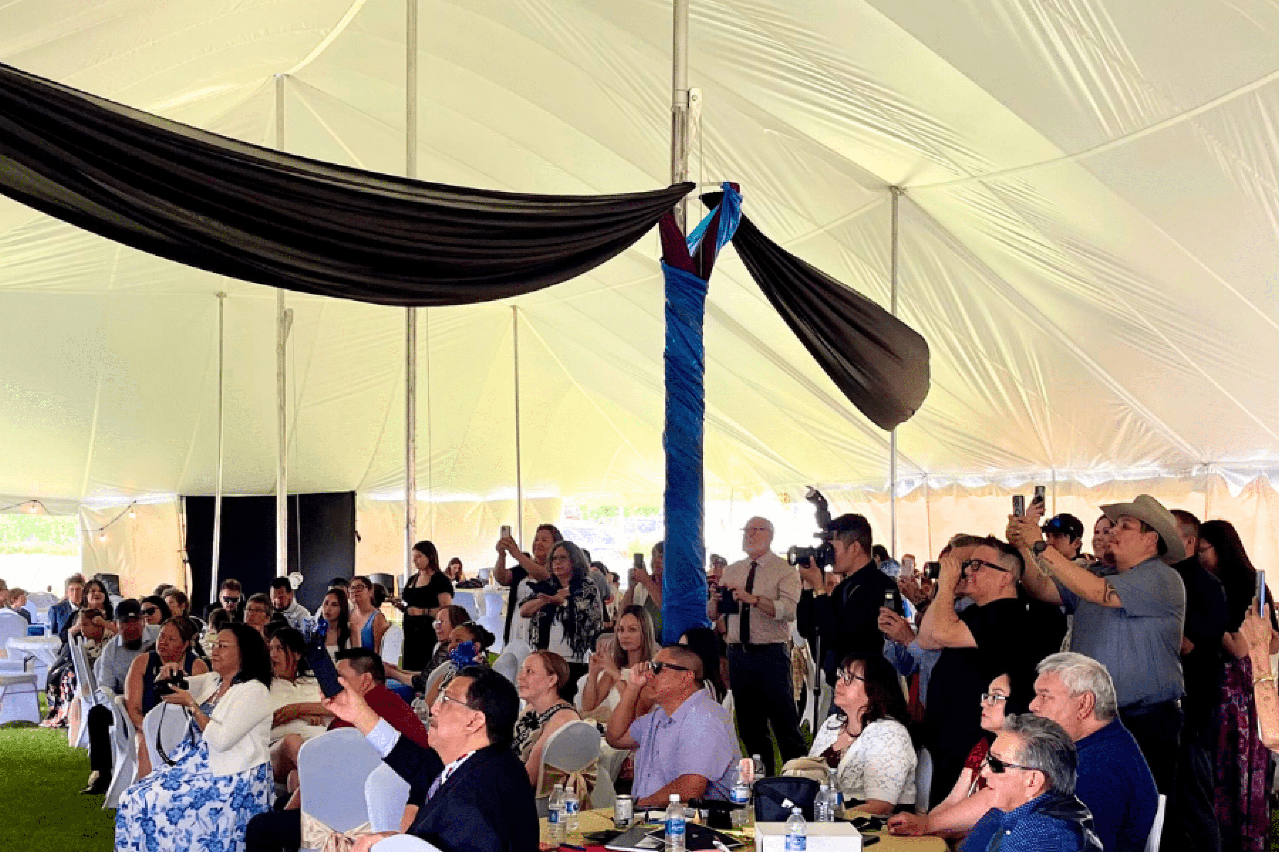 Family and guests watch the graduation ceremony under a large tent.