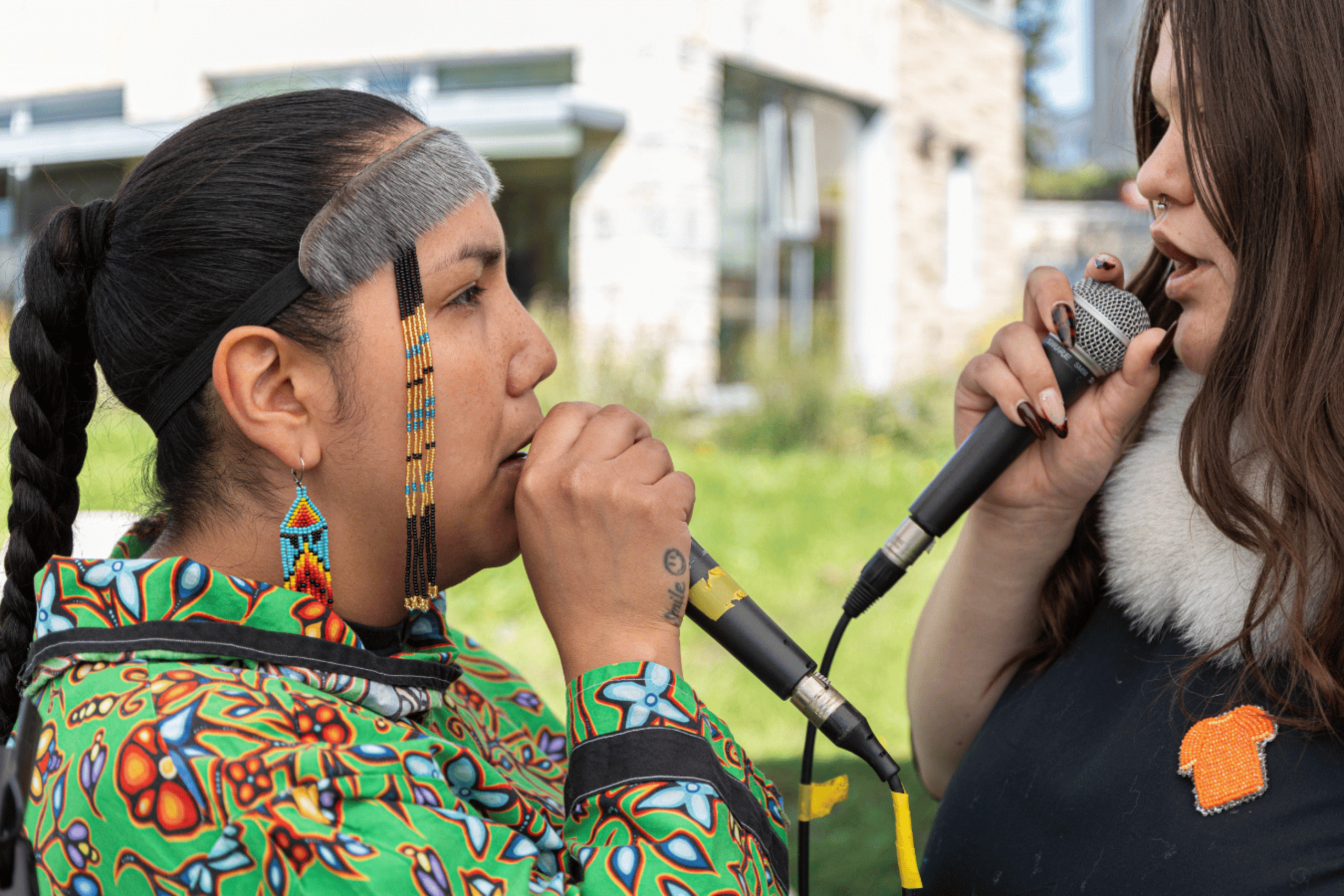 Two performers sing into microphones outdoors.