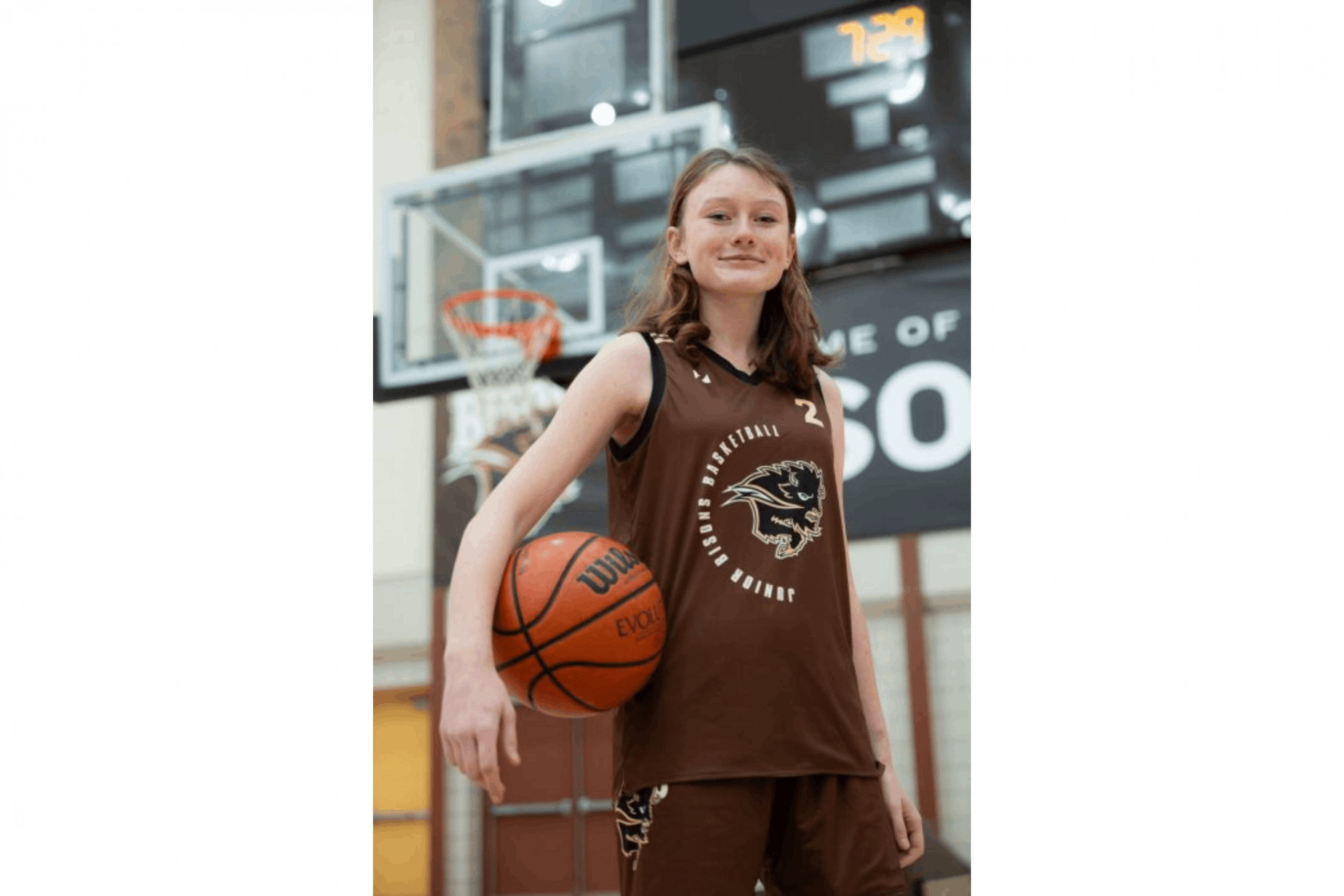 A junior bisons basketball player posing with a basketball, showing off the brown bisons basketball kit.