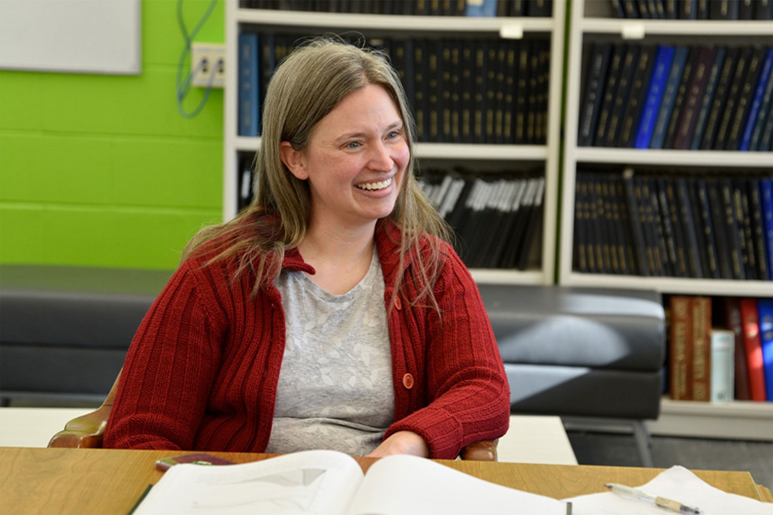 Katie Mitchell-Koch wearing a red cardigan with a book shelf background.