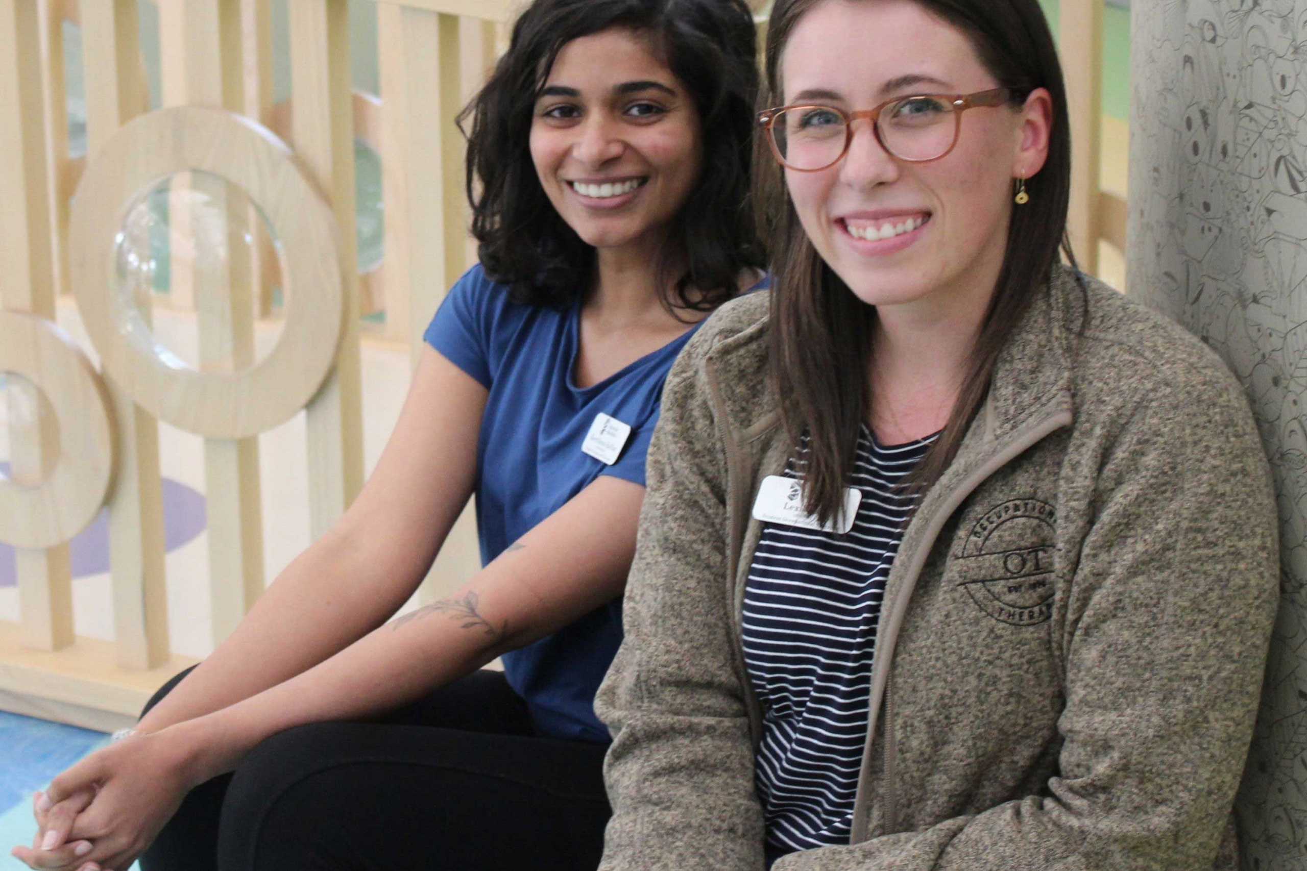 Keerthana Kalliat (left) and Lexie Rea (right), both sitting and smiling at the camera.