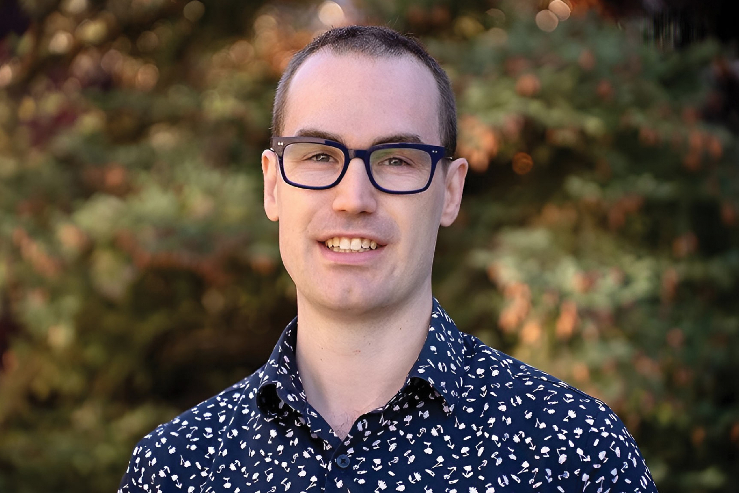 Kevin Mcgregor wearing a button down patterned shirt and eyeglass smiling at the camera.