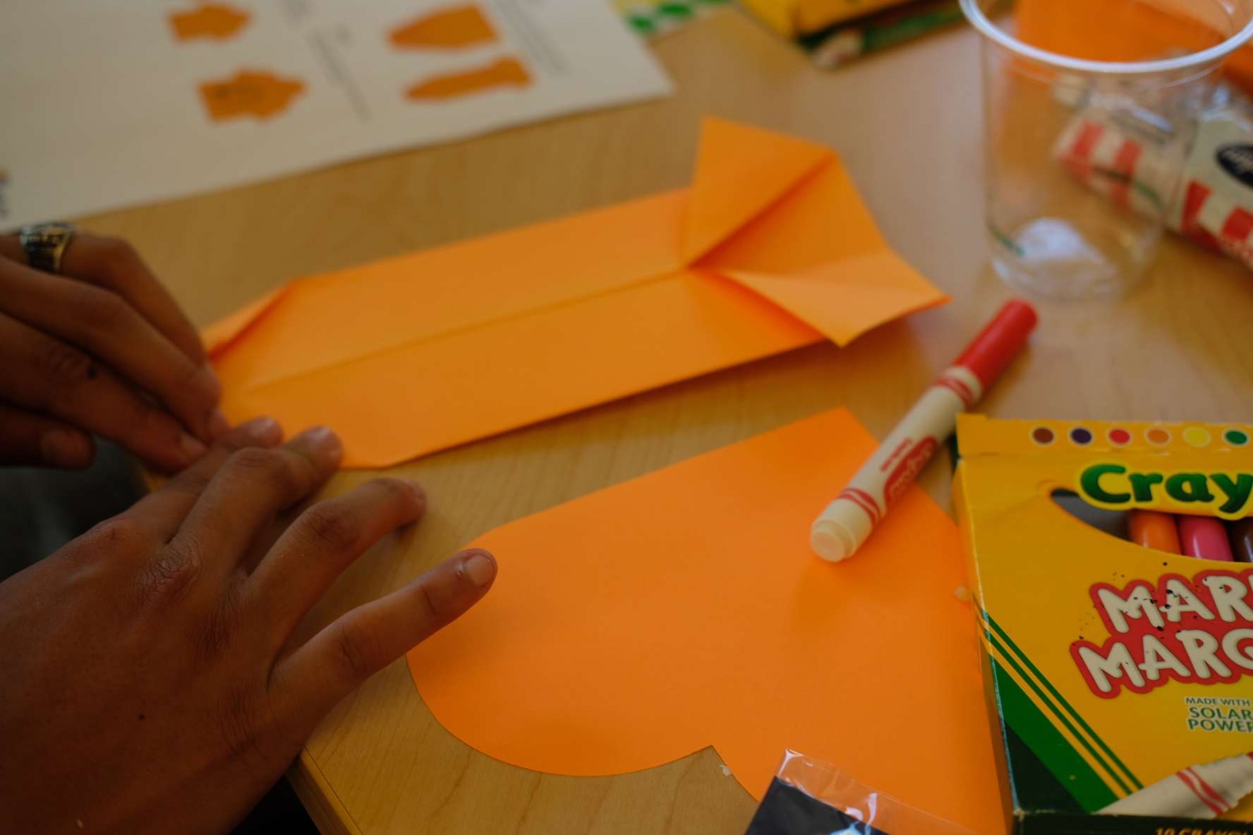 Hands folding orange paper into an origami shirt.