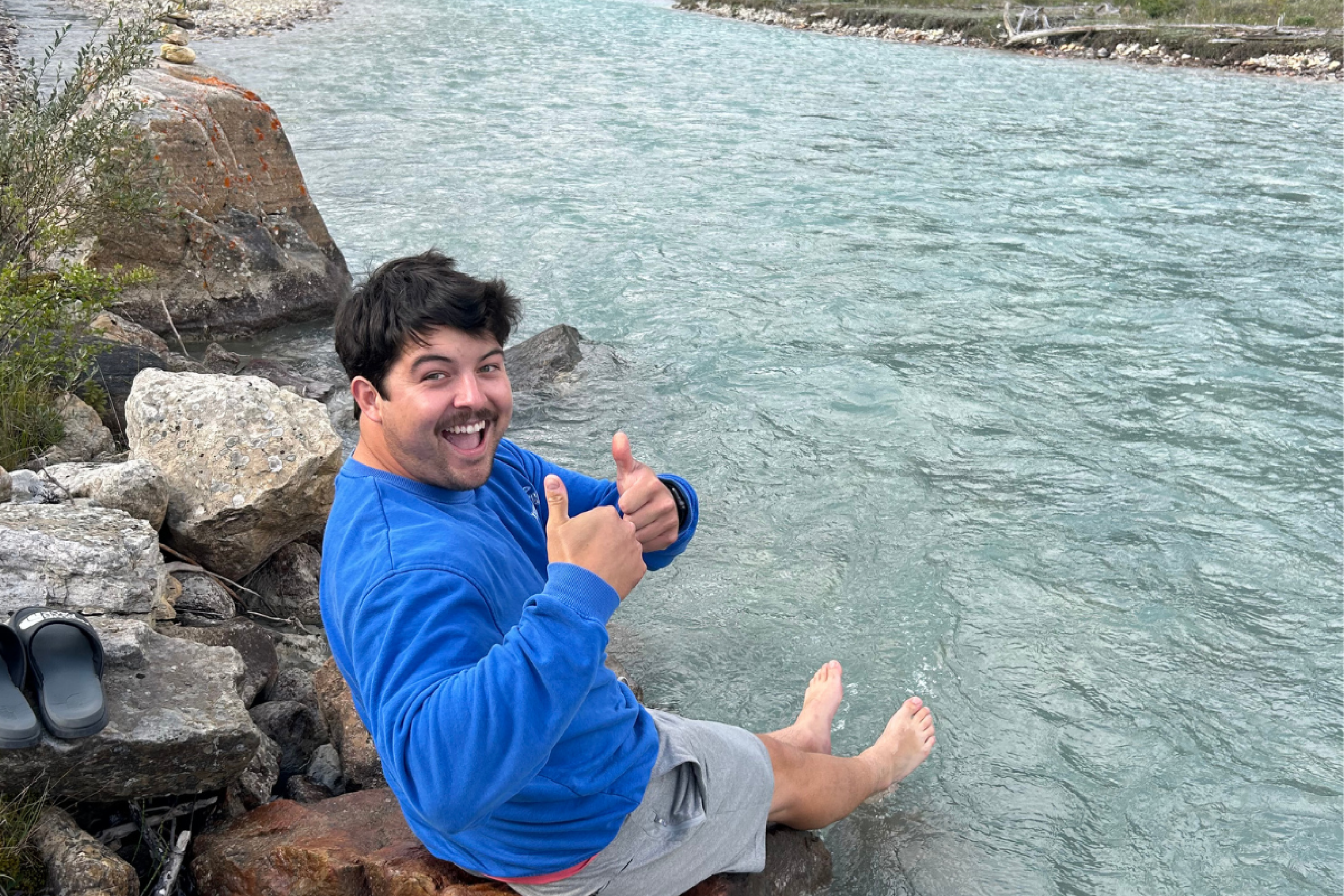male on a rock near lake giving thumbs up